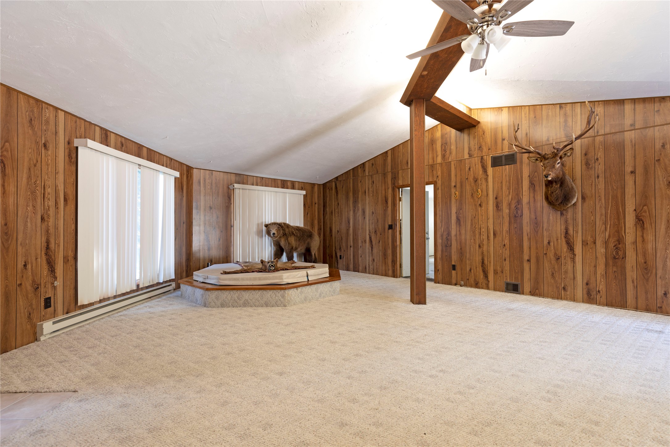 Wood-paneled room with a taxidermied bear on a raised platform and an elk head mounted on the wall.