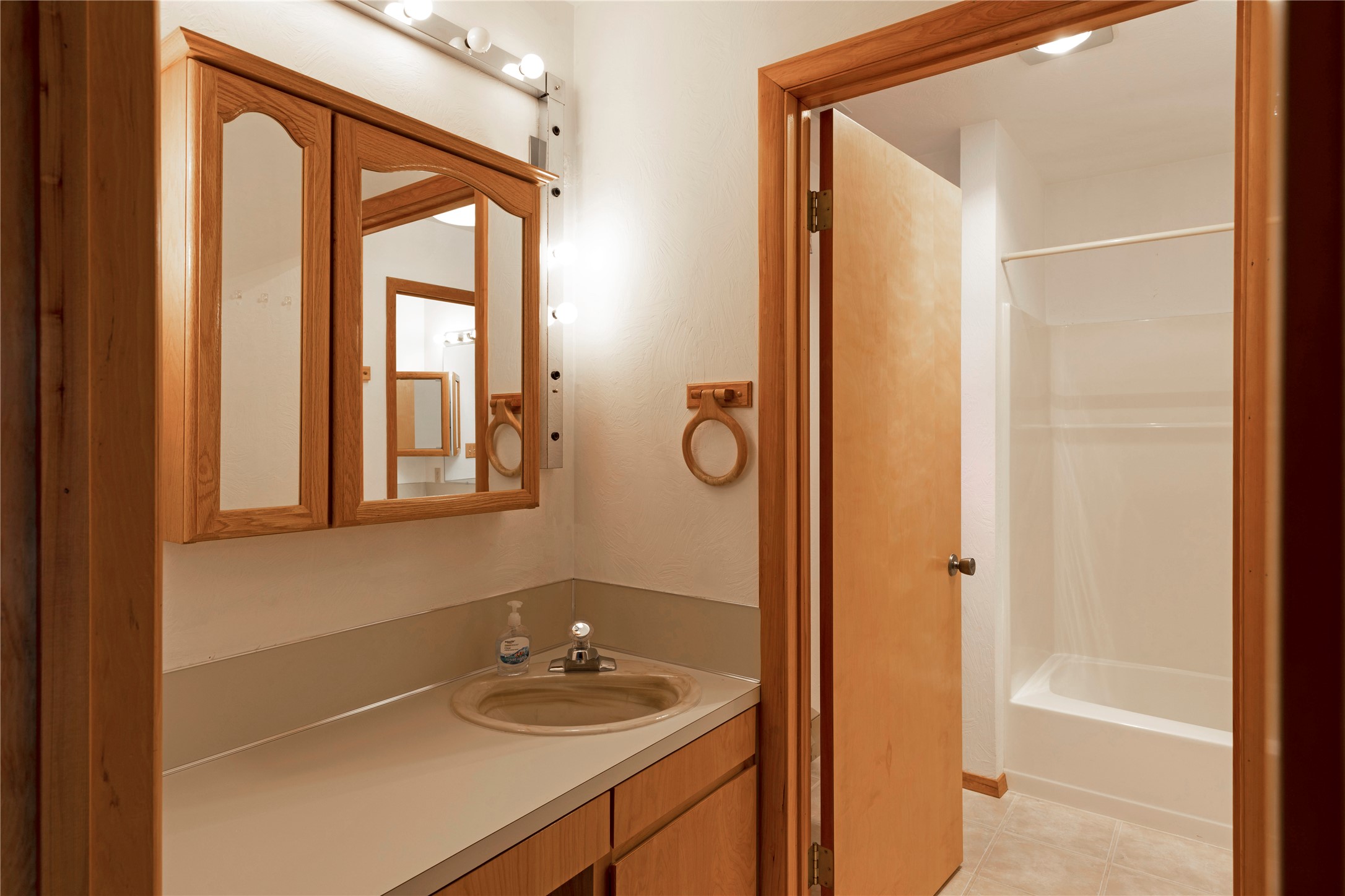 Bathroom with a wood-framed mirrored vanity and sink beside a bathtub and shower alcove.