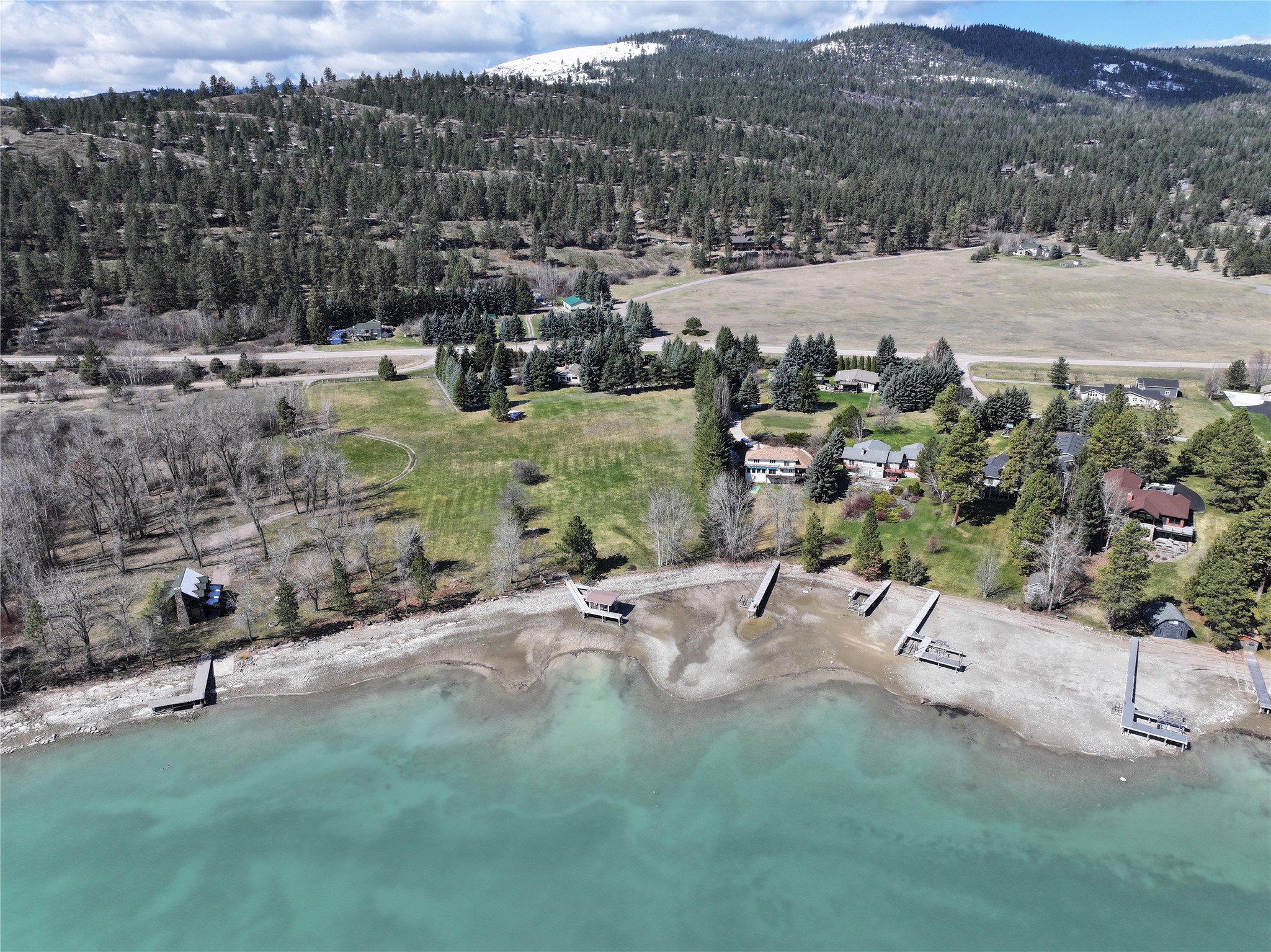 Aerial view of waterfront homes, private docks, lawns, and forested hills along turquoise water.