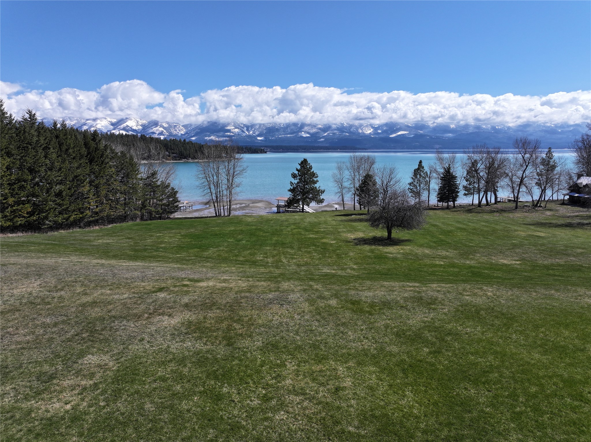 Waterfront property with a broad lawn, lakeshore docks, and snow-dusted mountains across the lake.
