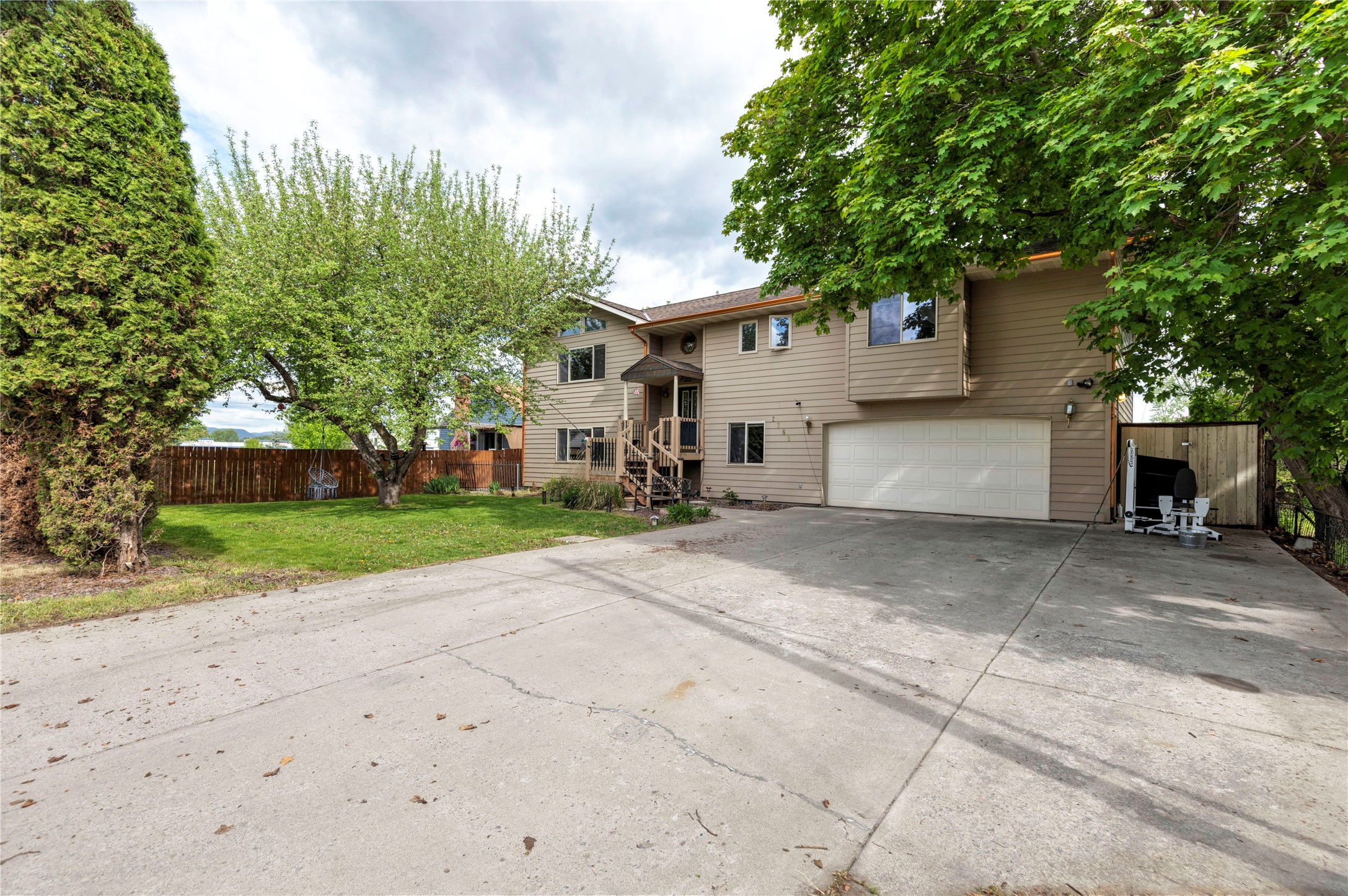 Beige two-story house with an attached garage, broad driveway, and mature trees.