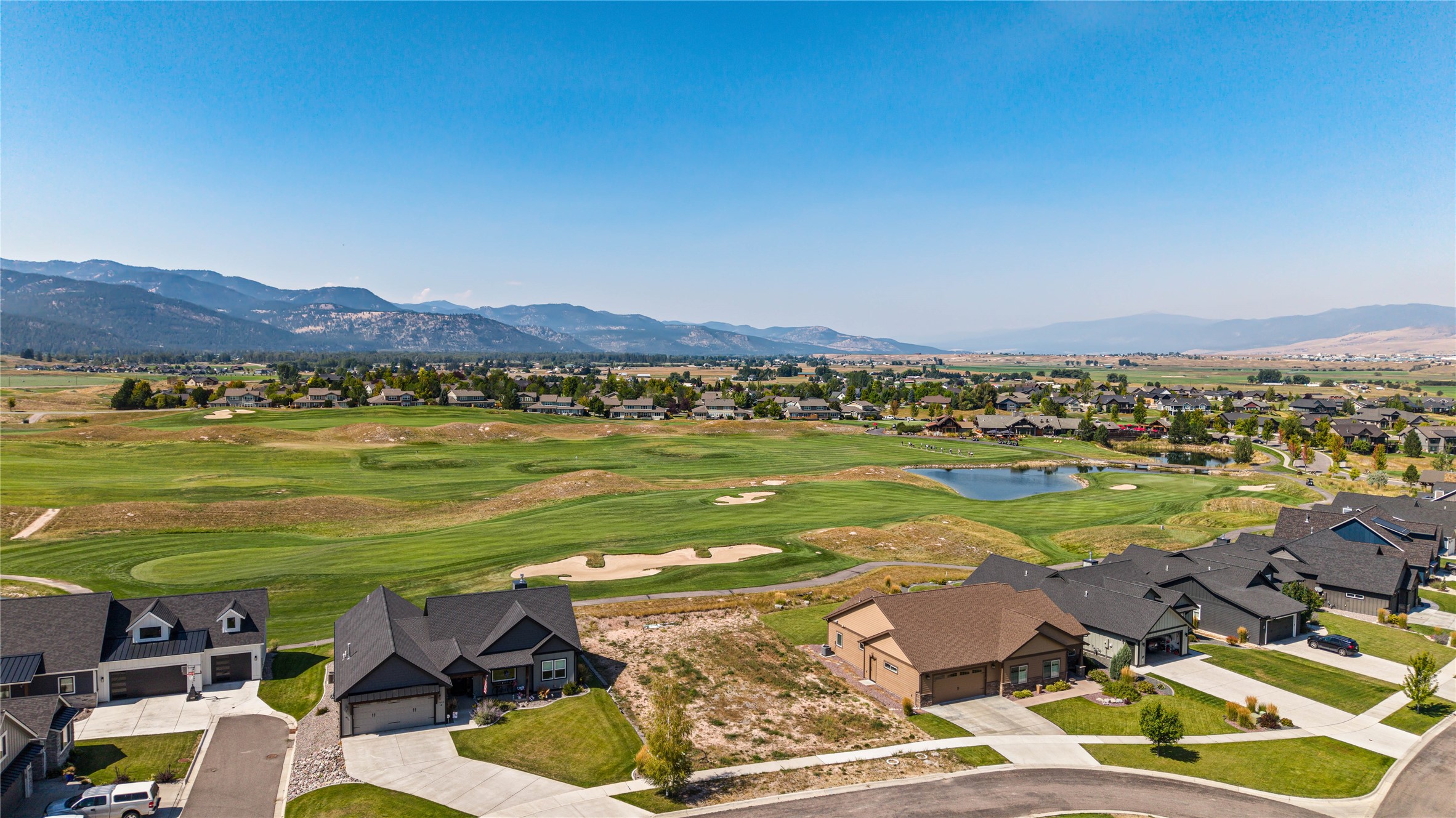Homes border a golf course with a pond and mountain range beyond.
