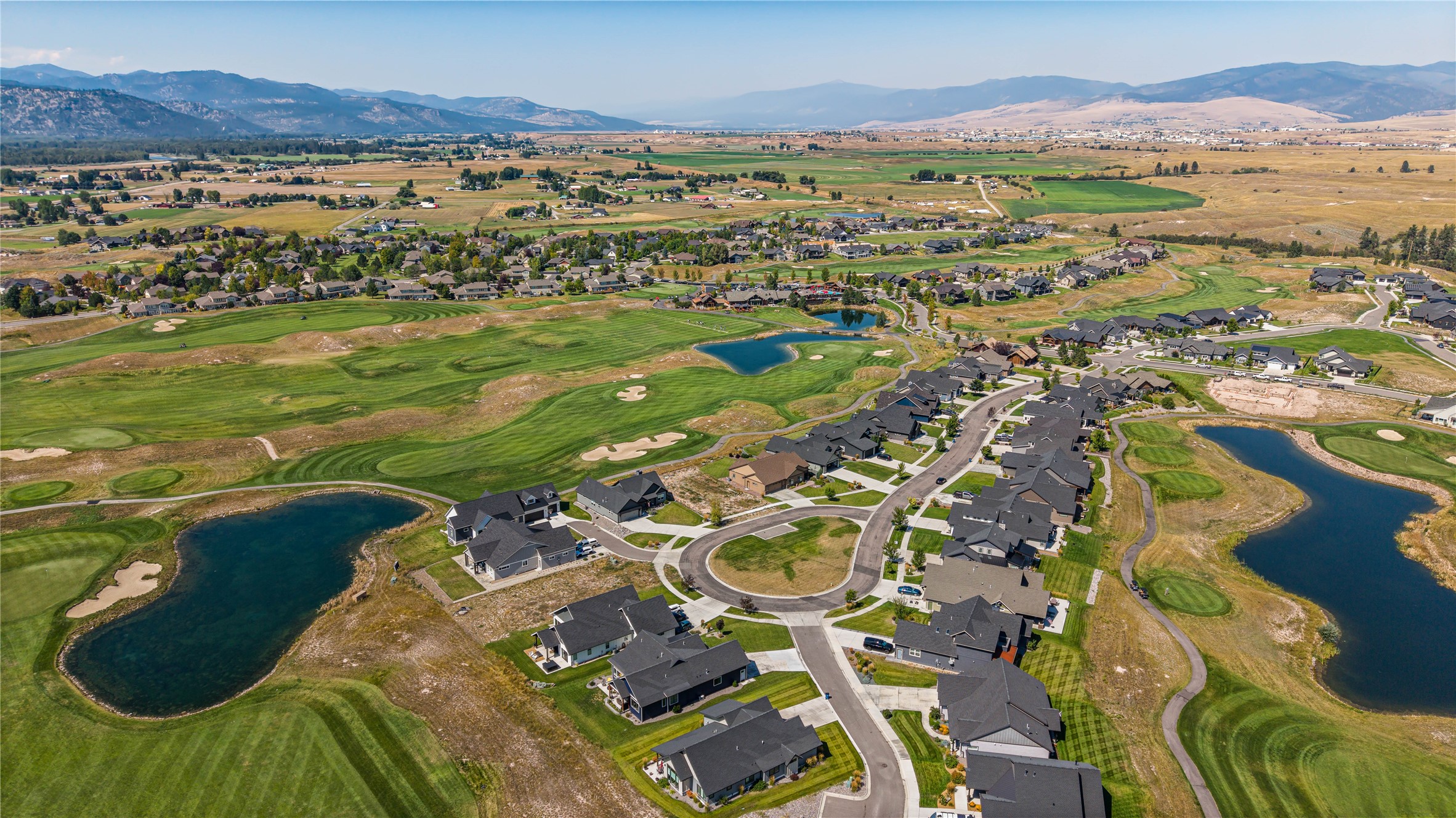 Aerial view of homes beside golf course fairways and ponds, with mountains in the distance.