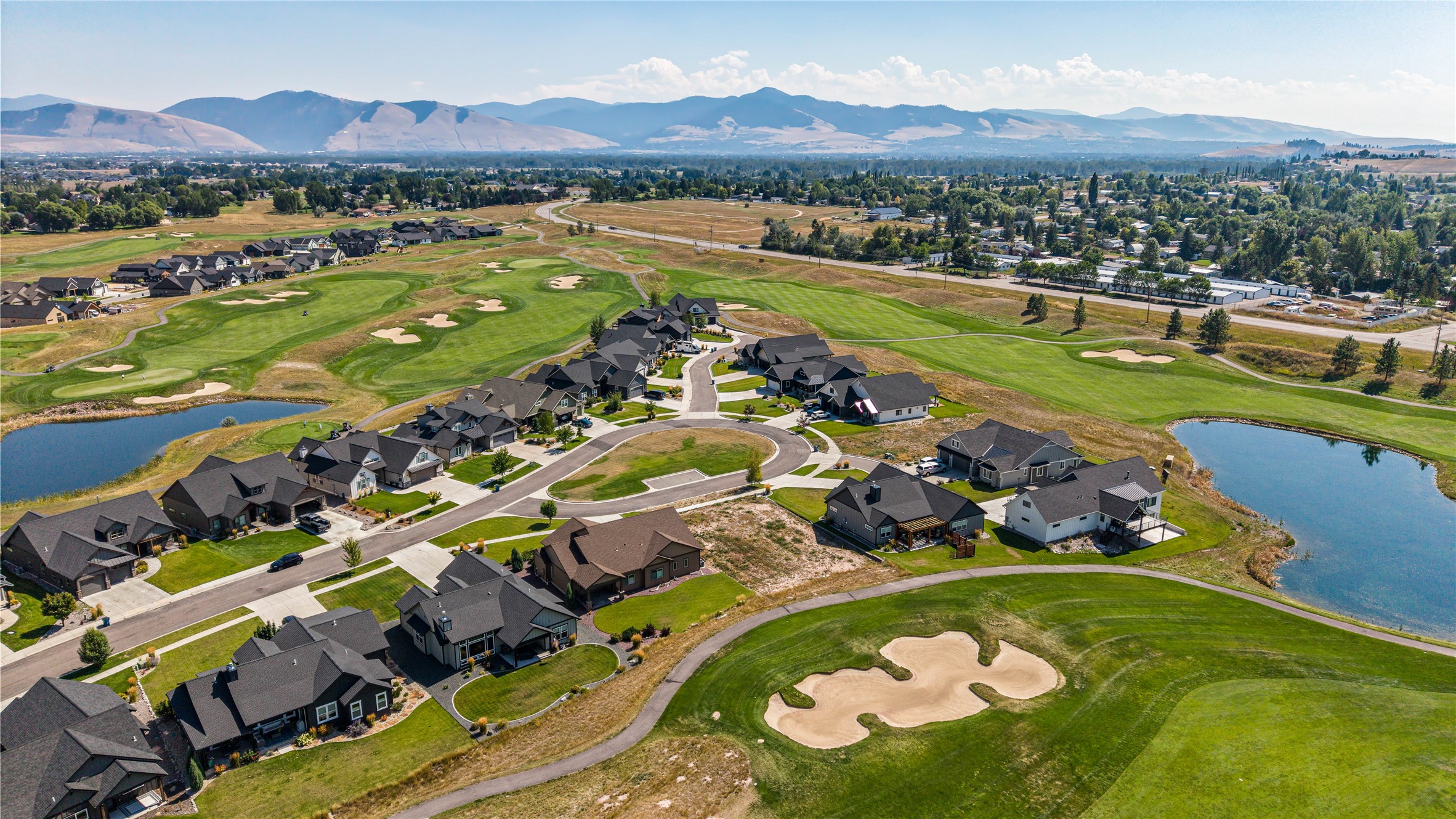 Aerial view of homes beside a golf course, with ponds and mountains in the distance.