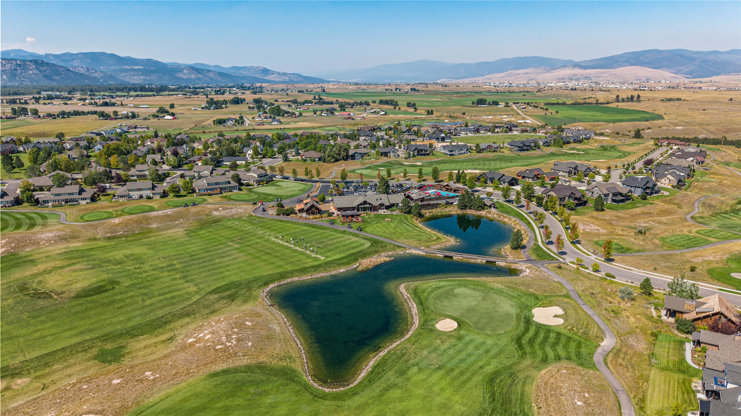 Aerial view of homes and golf course fairways surrounding ponds, with mountains in the distance.