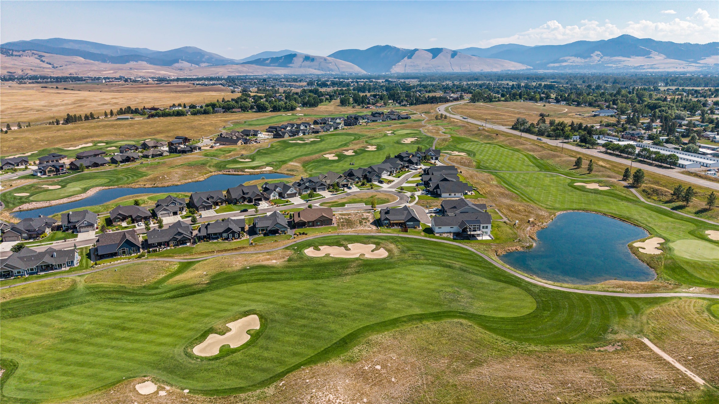 Aerial view of homes beside a golf course, ponds, and distant mountains.
