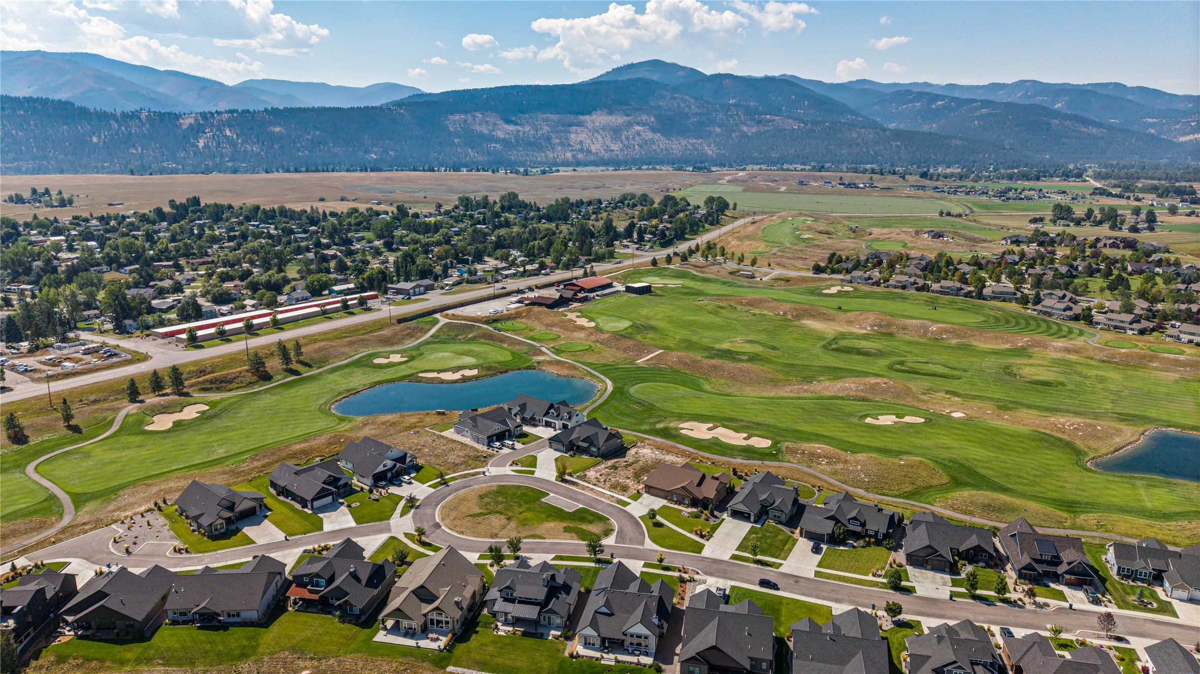 Aerial view of homes beside a golf course and pond, with mountains in the distance.