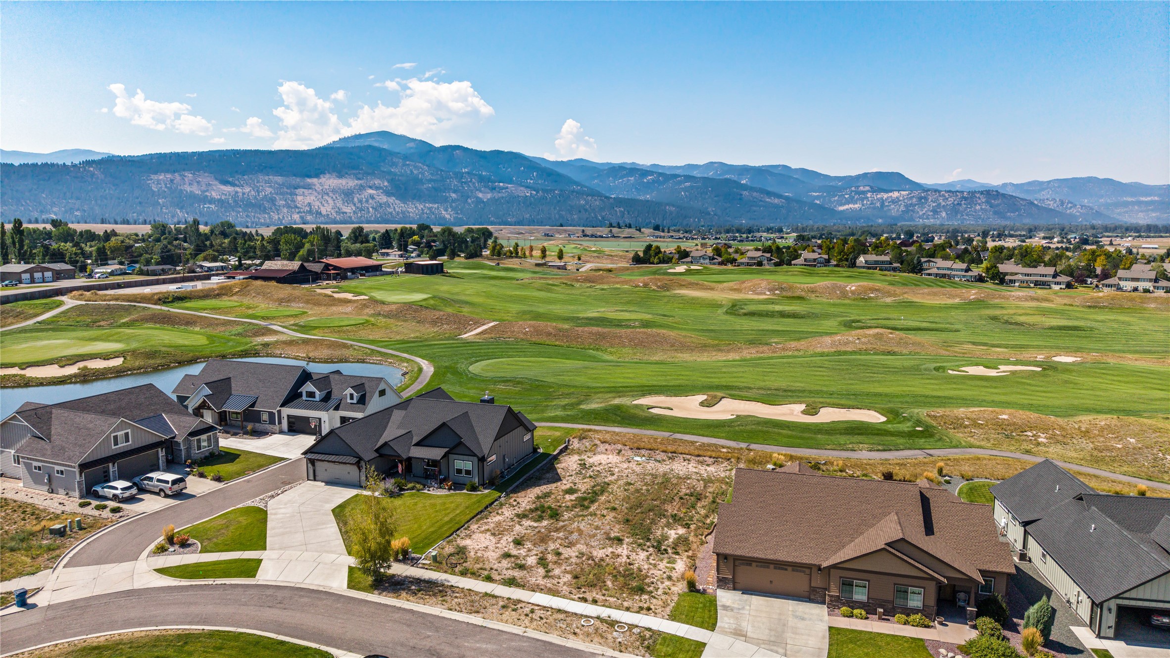 Aerial view of homes beside a golf course, with a pond and mountain range beyond.