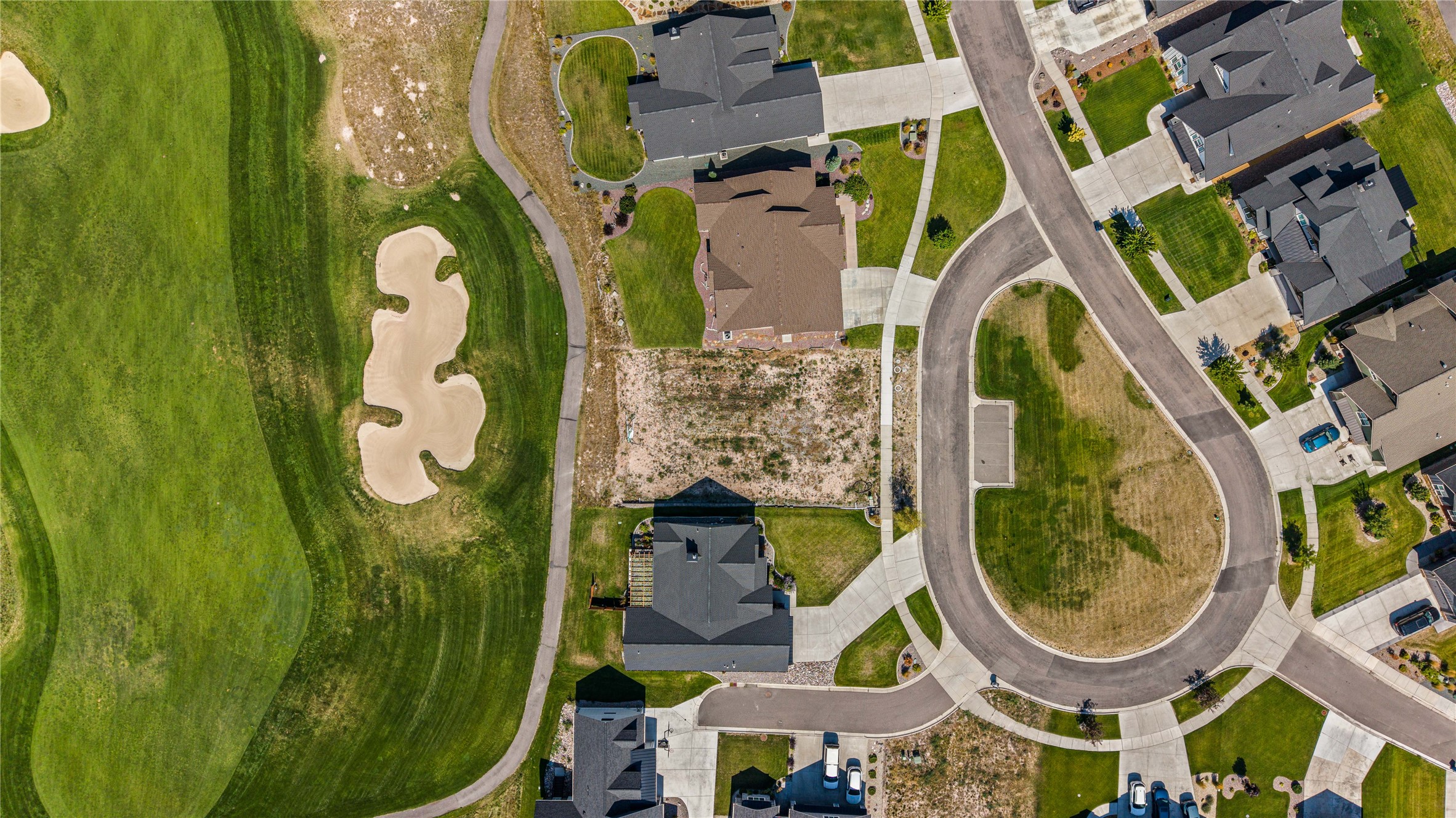 Aerial view of an undeveloped parcel beside a golf course and residential cul-de-sac.