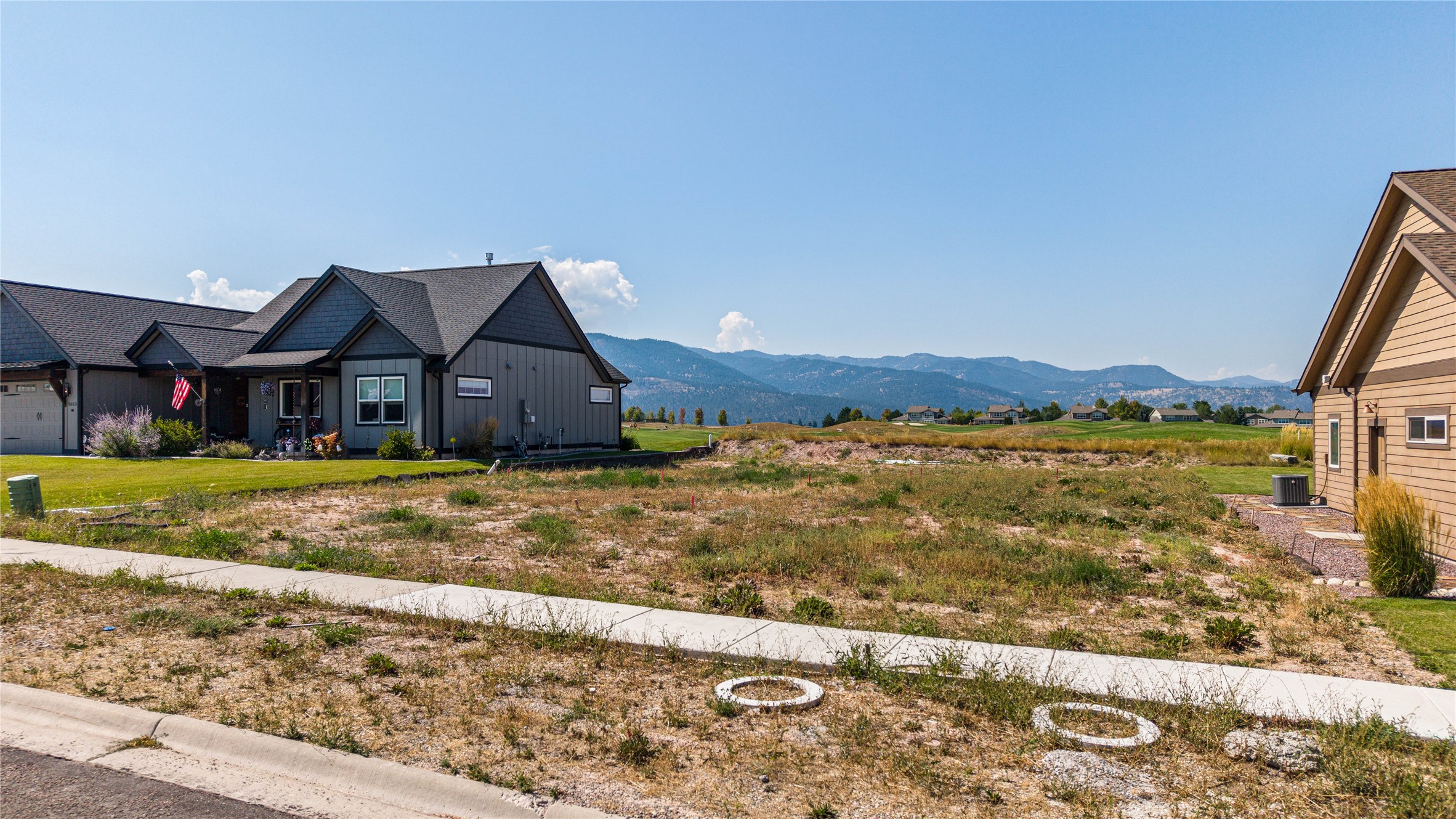 Vacant residential lot with neighboring homes and a mountain range in the distance.