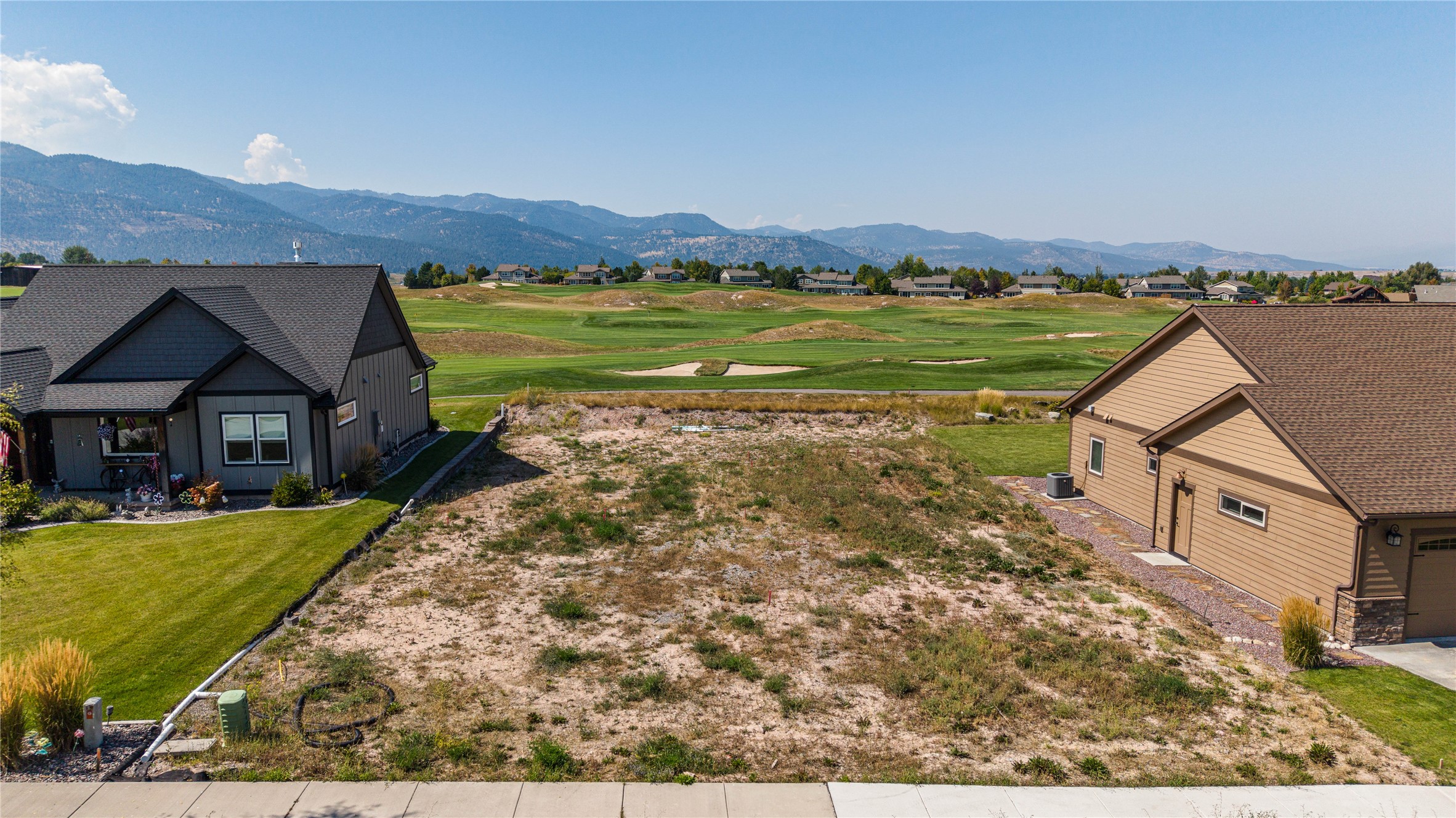 Vacant lot between homes overlooking a golf course and mountain range.