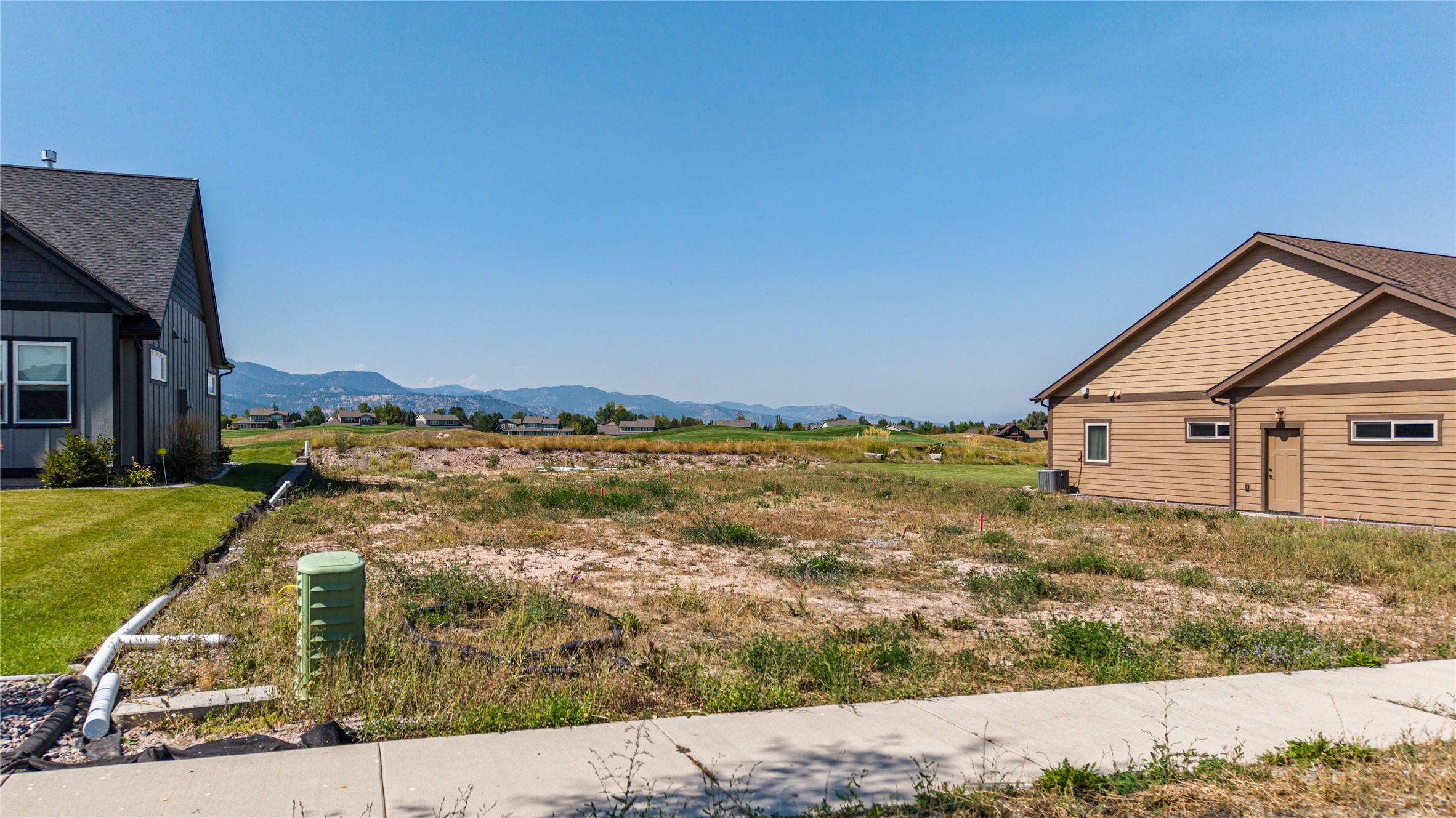 Vacant lot between two homes, with a sidewalk in front and mountains in the distance.