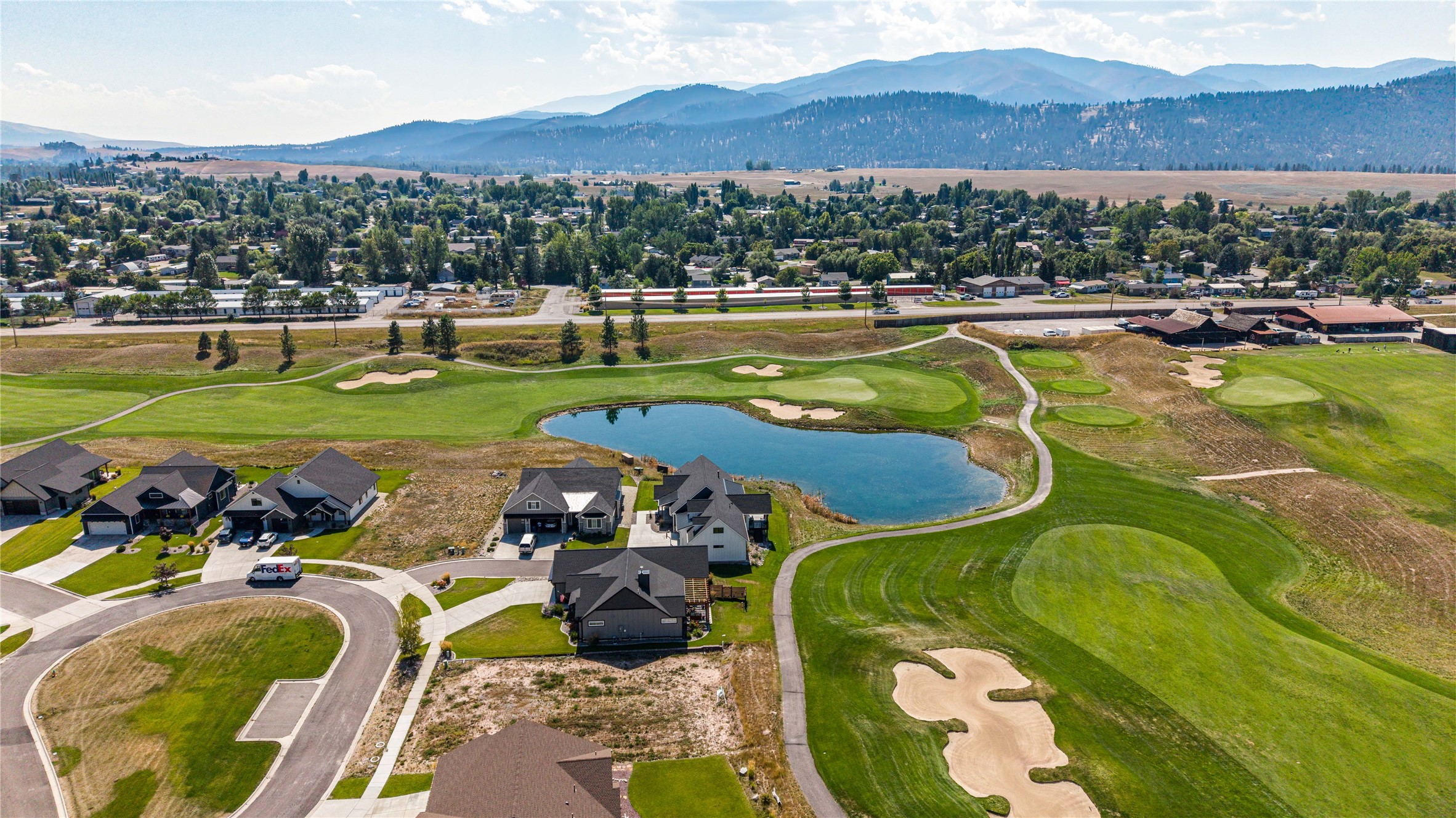 Aerial neighborhood view beside a golf course pond, with mountains beyond.