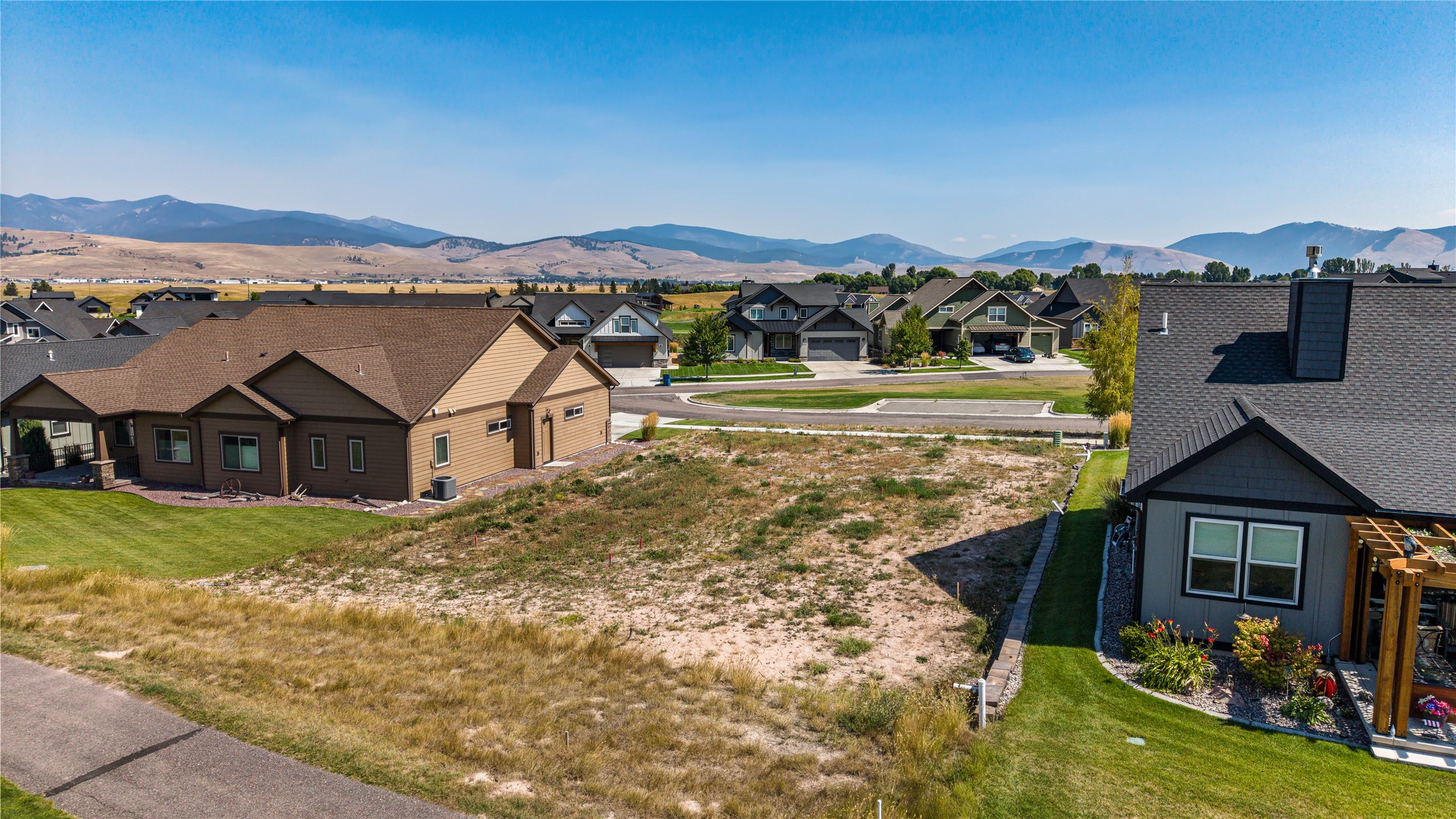Vacant residential lot between homes, with mountains rising beyond the neighborhood.