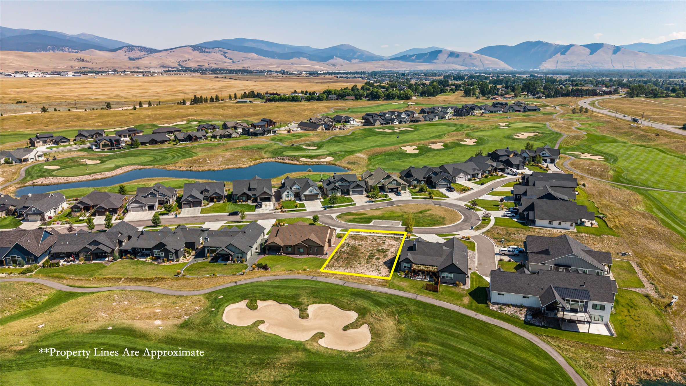 Vacant lot outlined in yellow beside homes and golf fairways, with mountains in the distance.