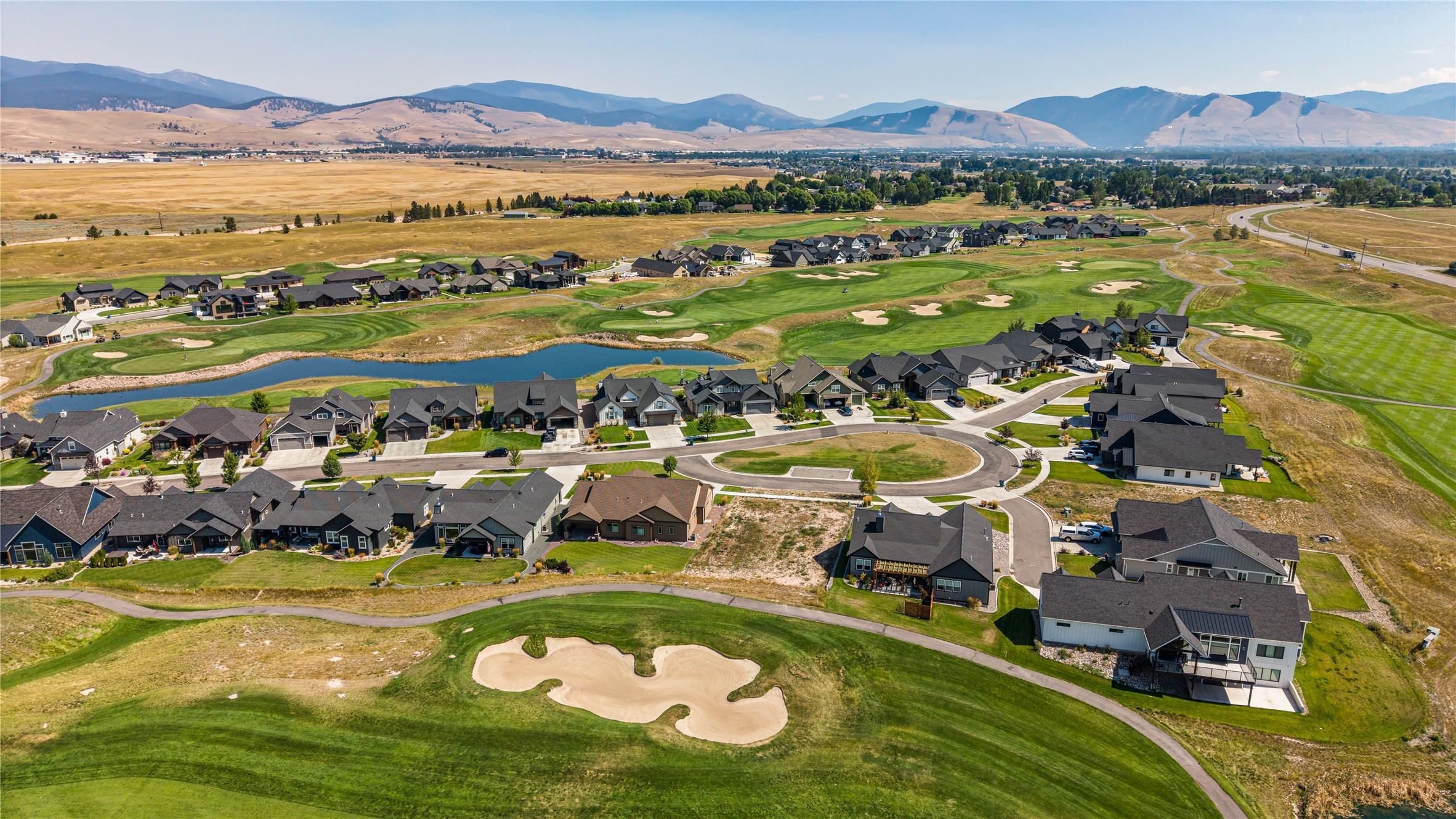 Aerial view of homes beside a golf course, with a pond and mountains beyond.