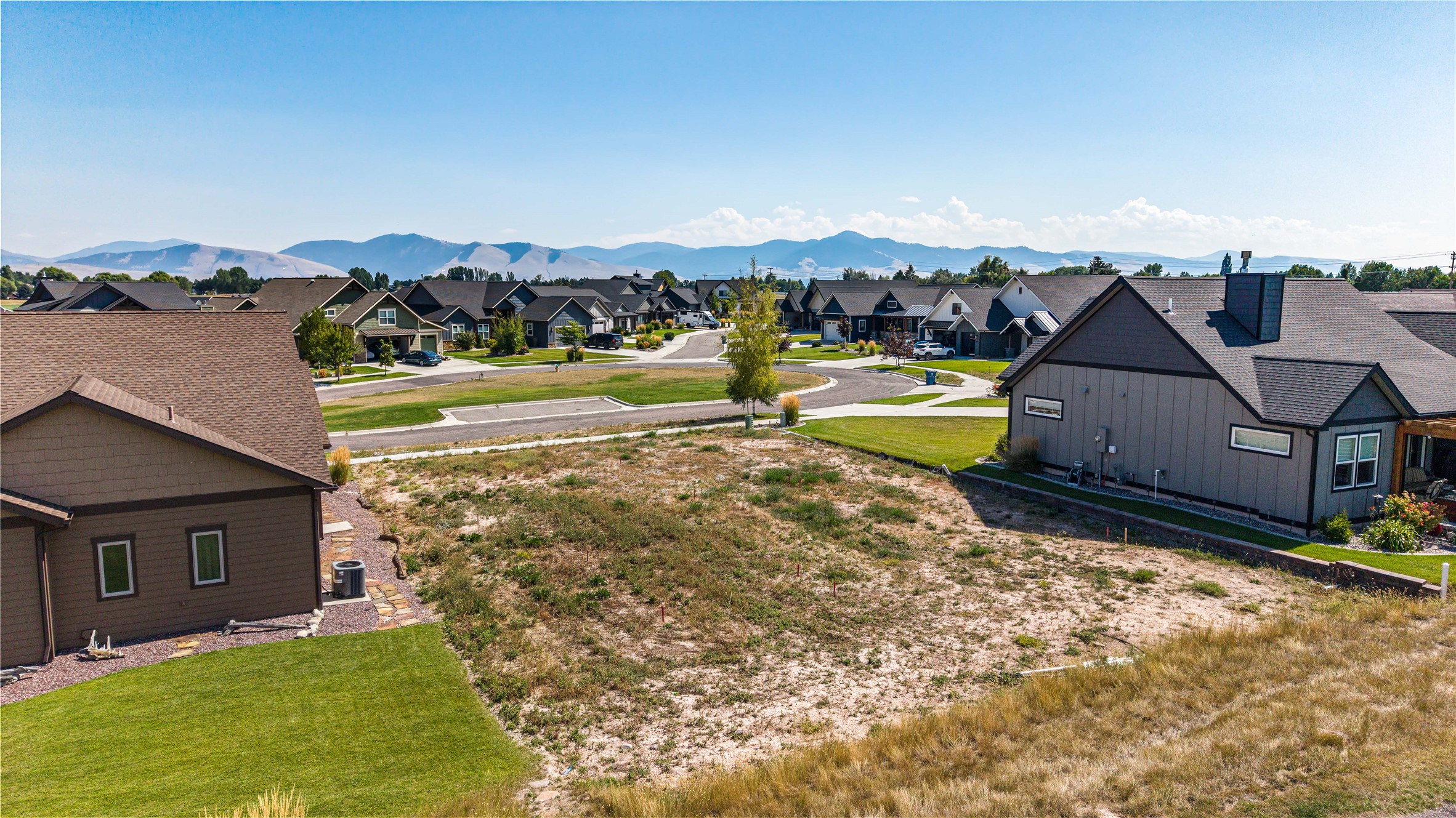 Vacant residential lot among neighborhood homes, with mountains in the distance.