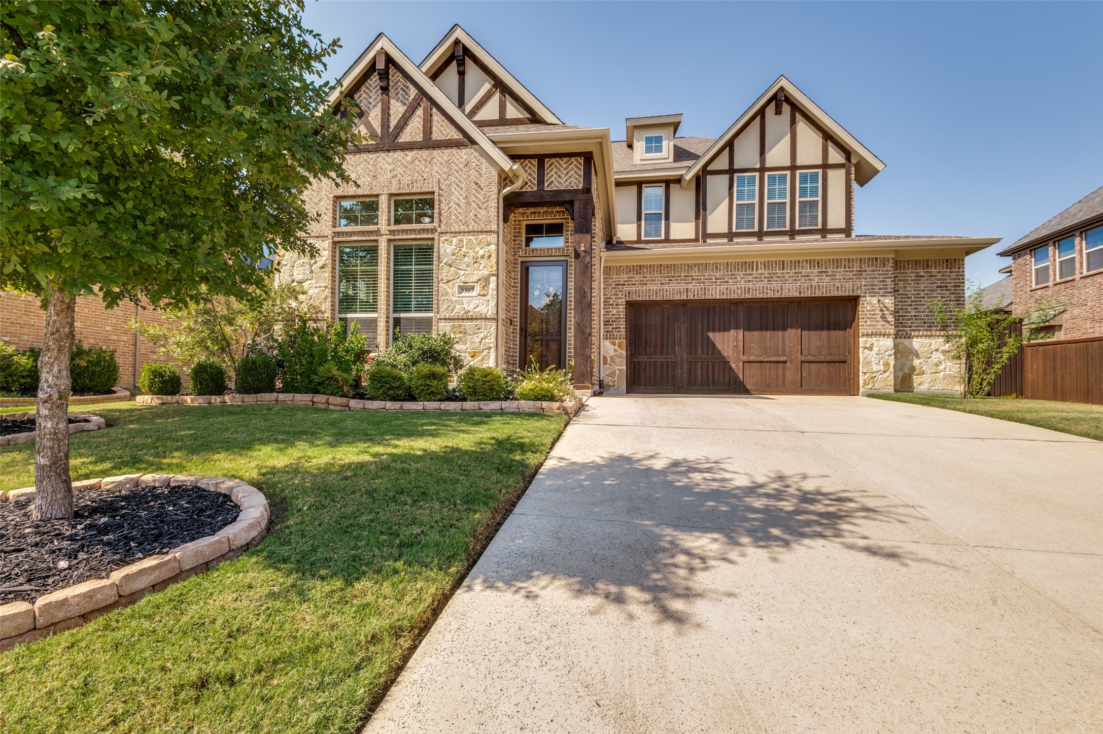 Two-story brick and stone house with timber-trimmed gables, landscaped lawn, and wide driveway.