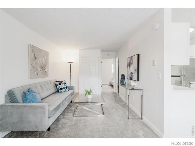 Living room with a gray sofa, glass coffee table, and open doorway to the bedroom.