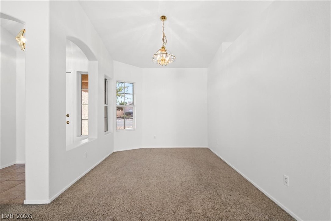 Empty carpeted dining room with a chandelier, two windows, and an arched opening.