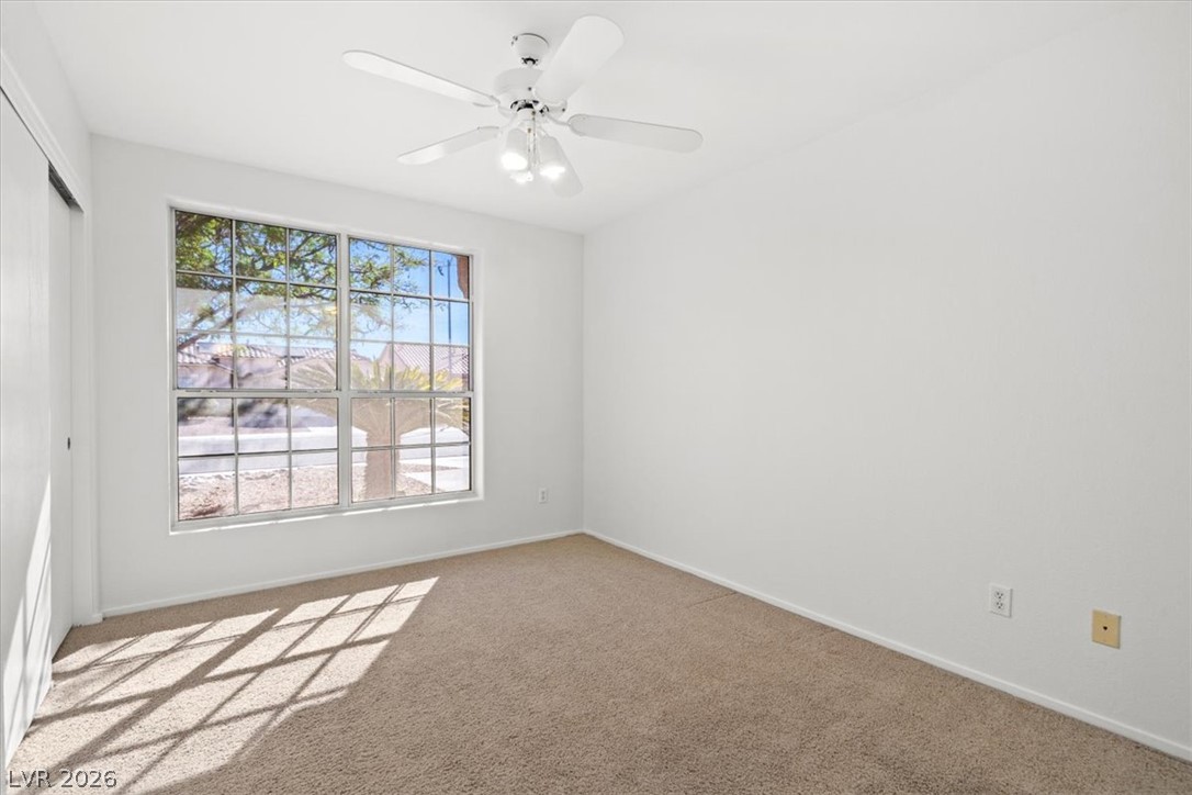 Empty bedroom with beige carpet, a ceiling fan, and a large window.