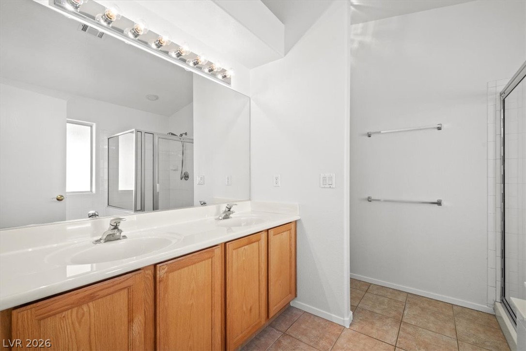 Bathroom with a double-sink vanity, honey-colored cabinets, and glass-enclosed shower.
