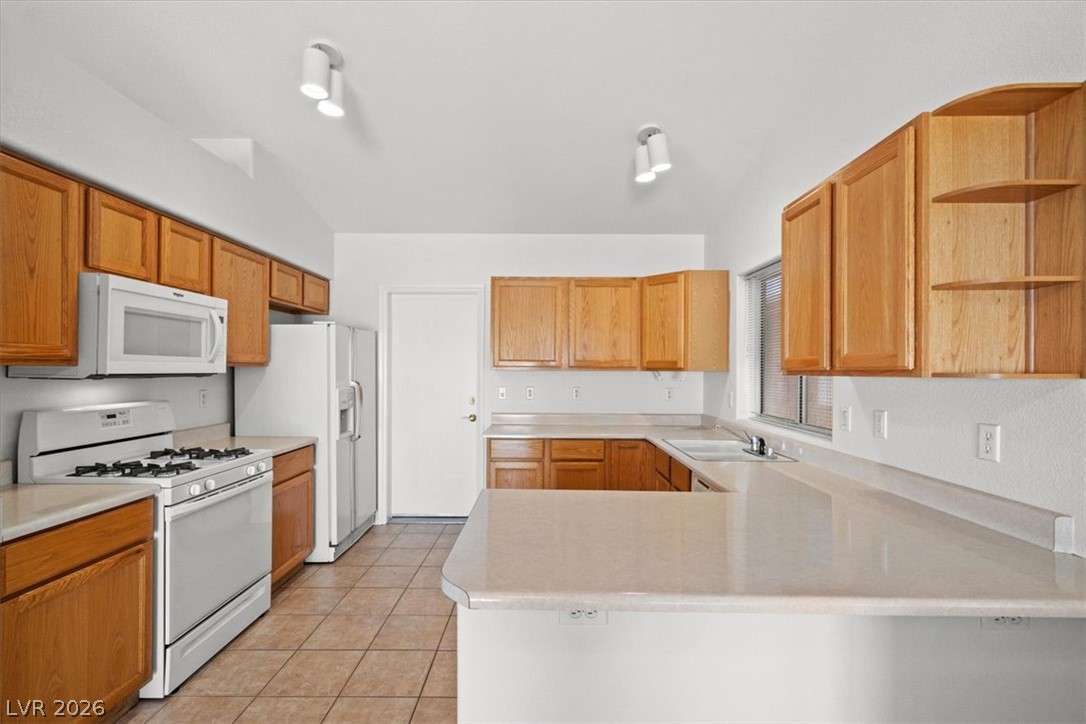 Kitchen with honey-toned cabinets, white appliances, and a large pale-countertop peninsula.