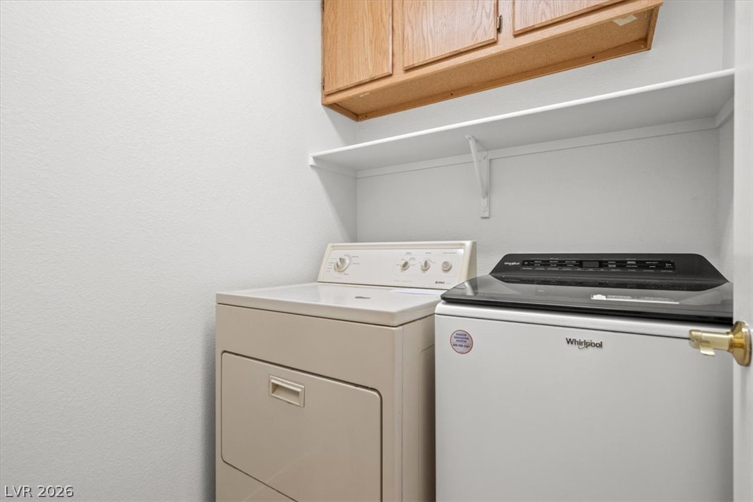 Laundry room with a Whirlpool washer and dryer beneath a shelf and wood cabinets.