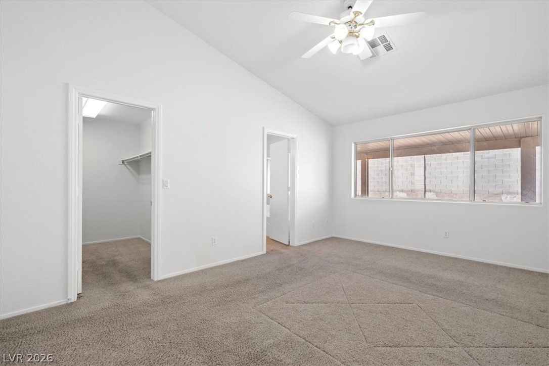 Vacant bedroom with beige carpet, ceiling fan, wide window, and open closet.