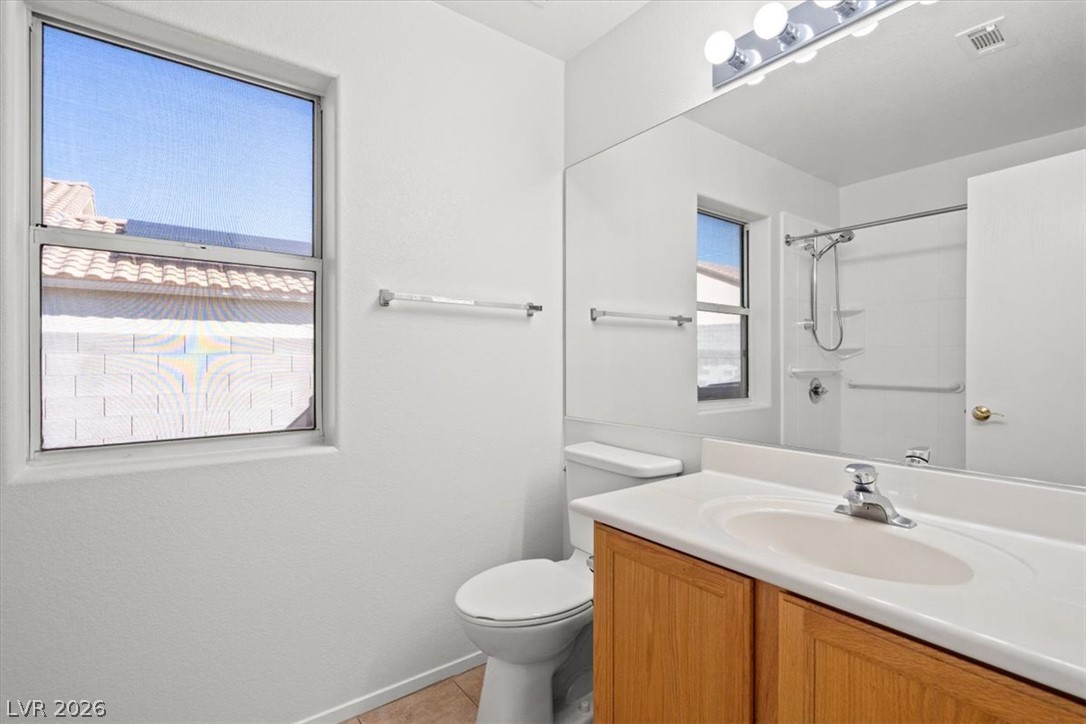 Bathroom with a wood-front vanity, large window, mirrored wall, and tiled shower with grab bars.