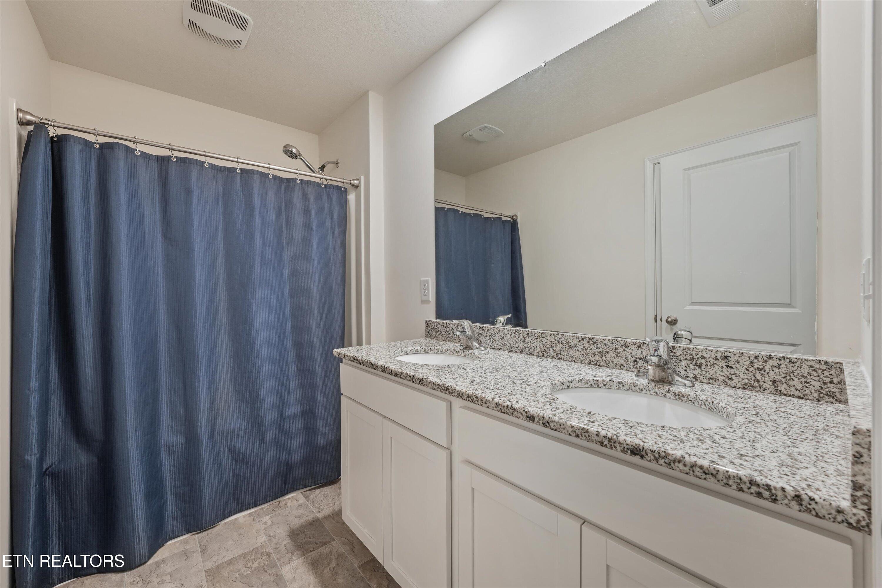 Bathroom with a double-sink granite vanity and blue shower curtain.