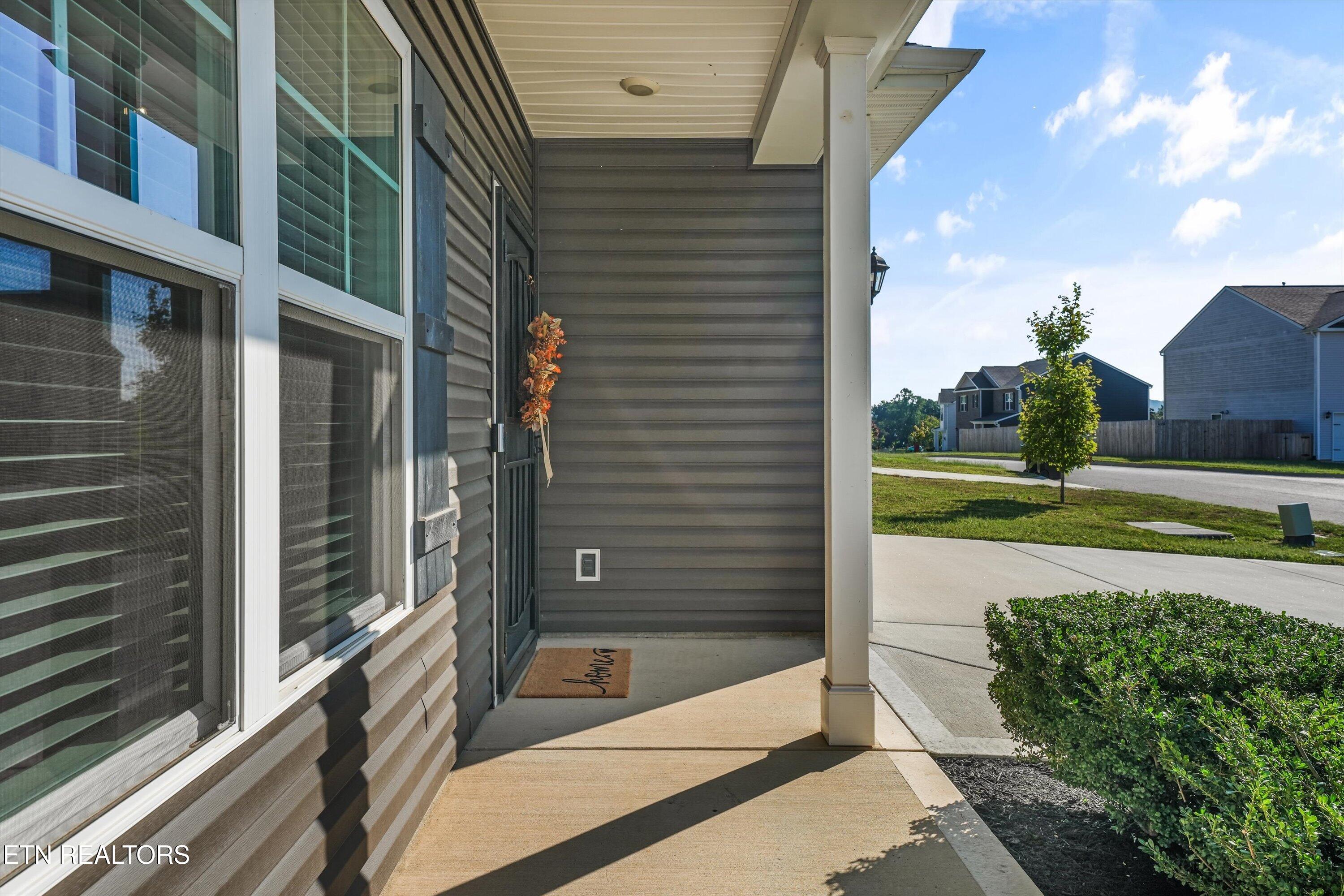 Covered front porch with gray siding, large windows, a wreath, and a view of the neighborhood.