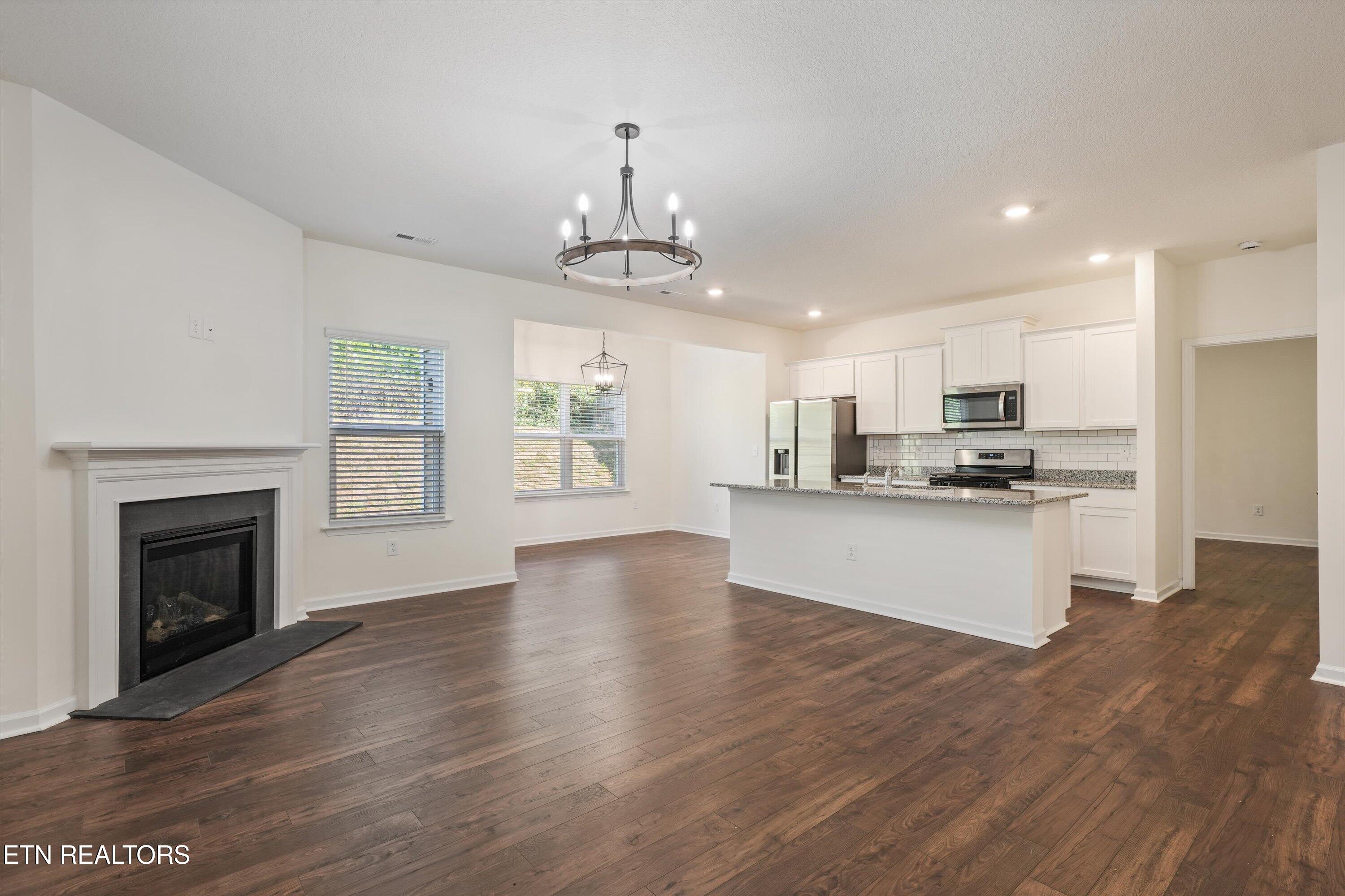 Open living room and kitchen with a gas fireplace, granite island, white cabinets, and dark wood floors.