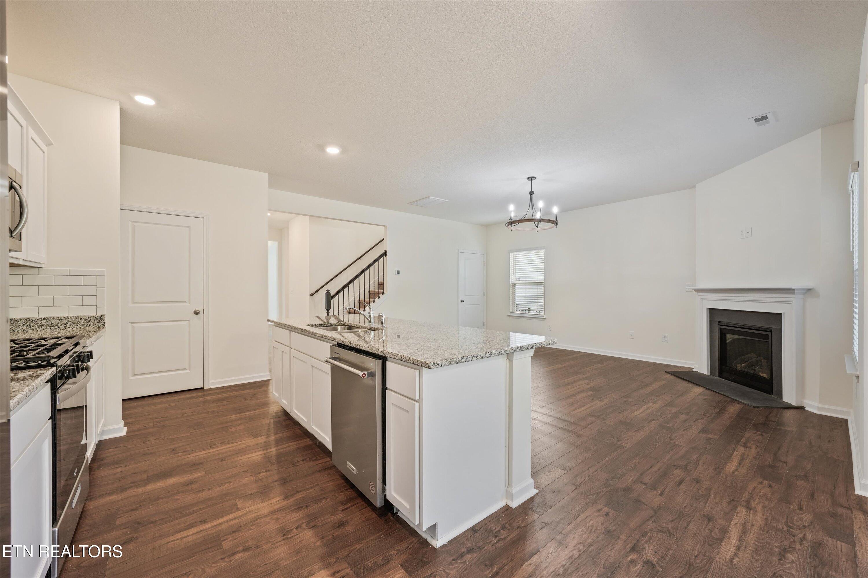 Open kitchen and living area with a granite island, dark wood floors, and a fireplace.