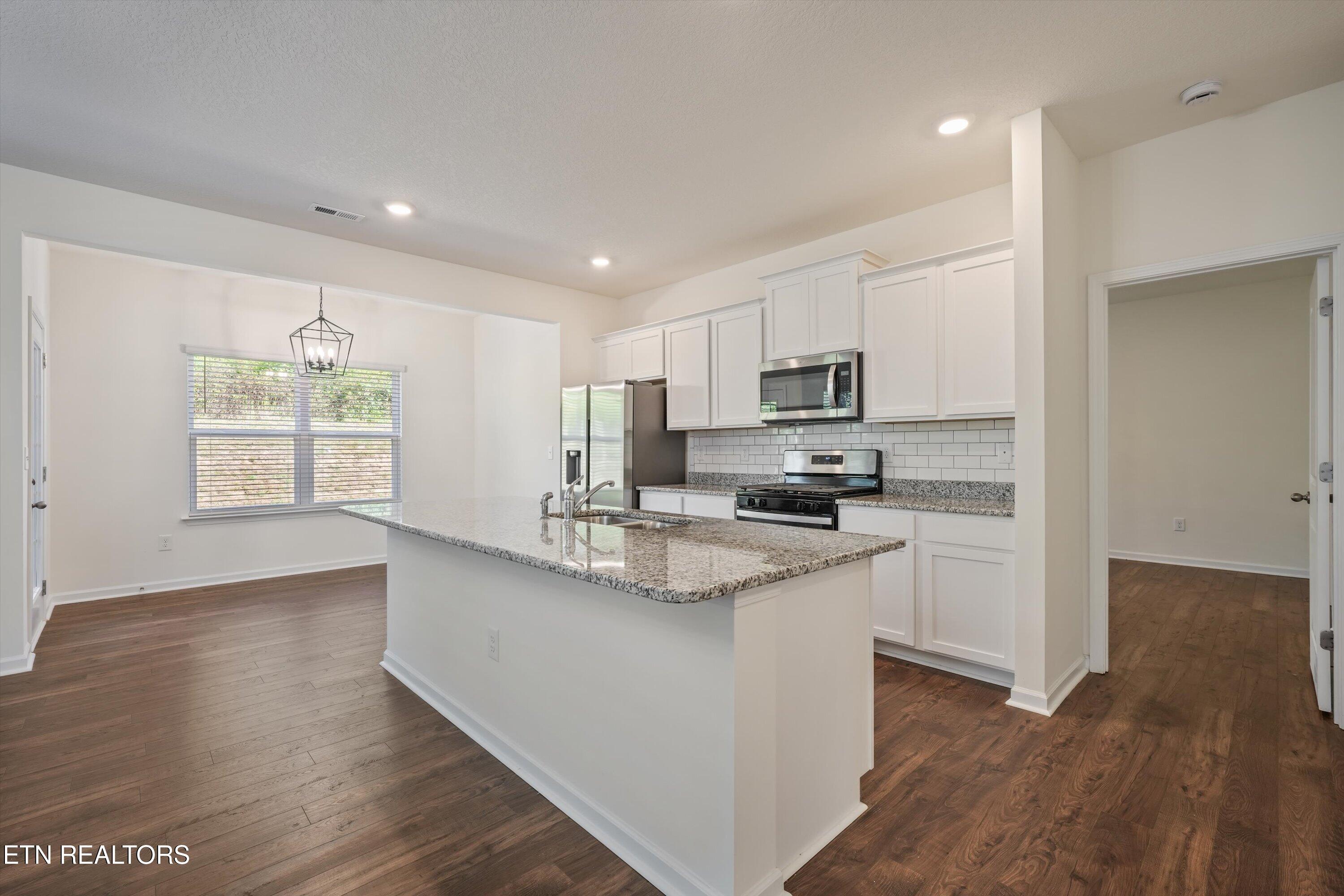Open kitchen with a large granite island, white cabinets, stainless steel appliances, and adjoining dining area.