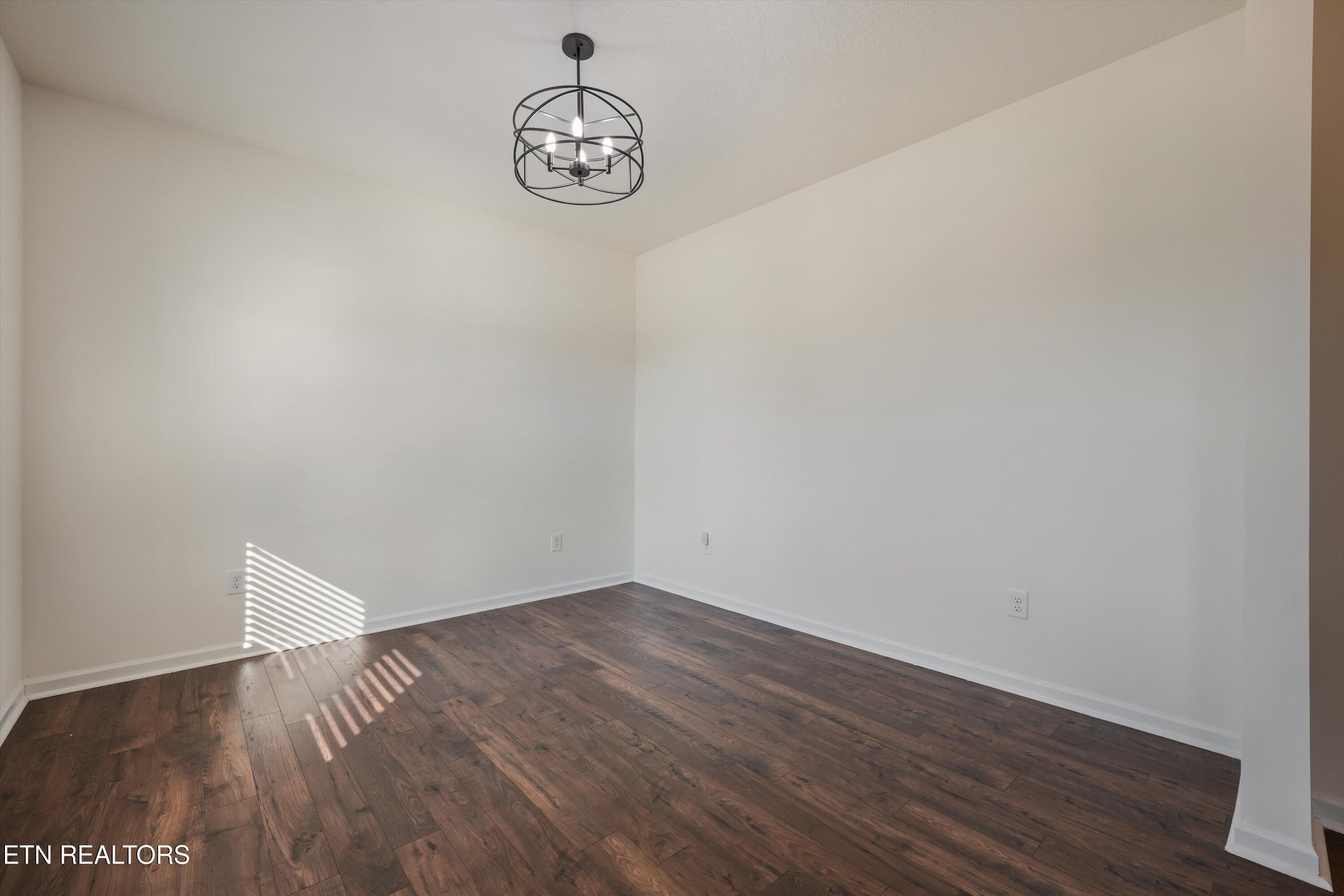 Vacant room with dark hardwood floors, white walls, and a black metal chandelier.