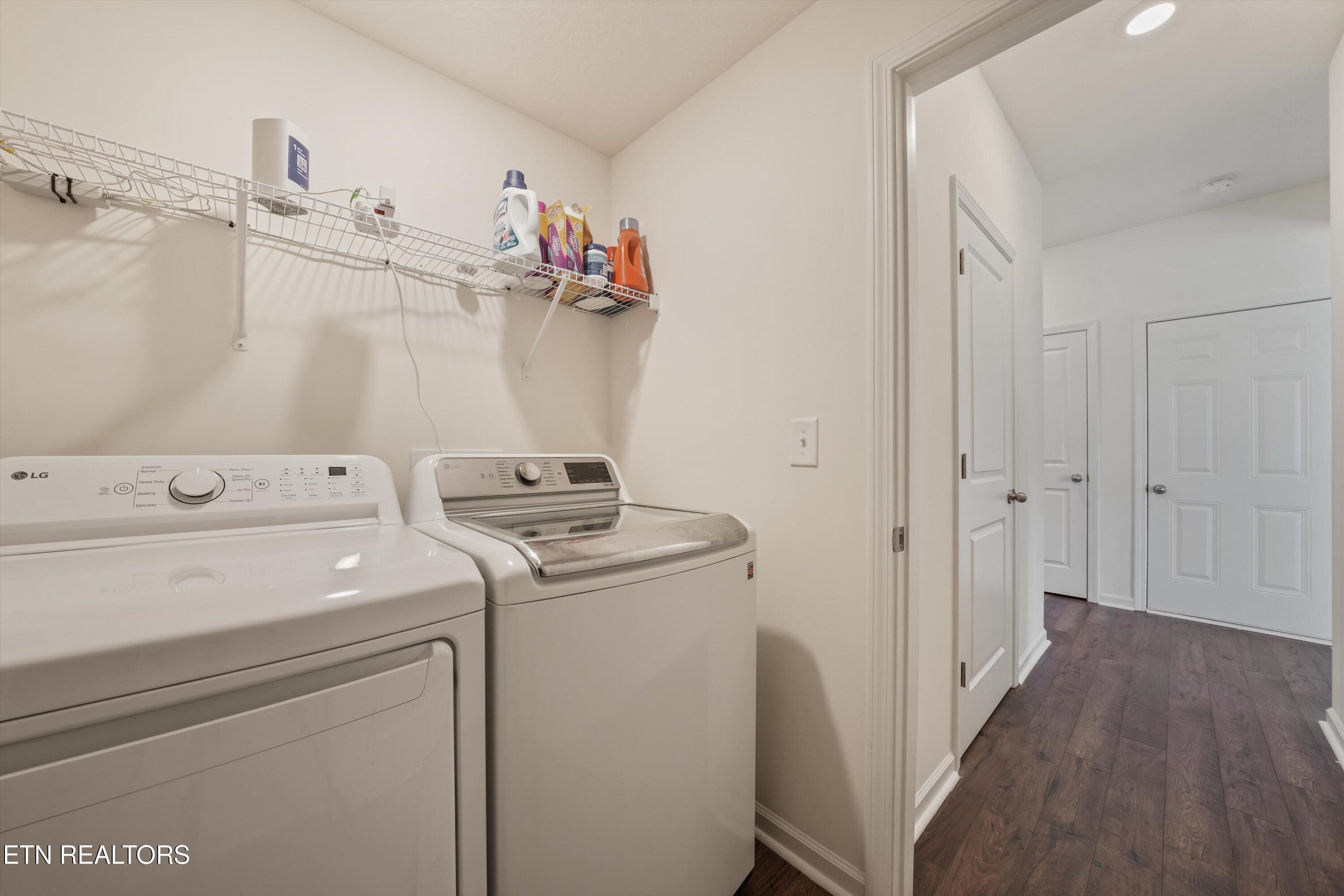 Laundry room with white washer and dryer, wire supply shelves, and a view into the hallway.