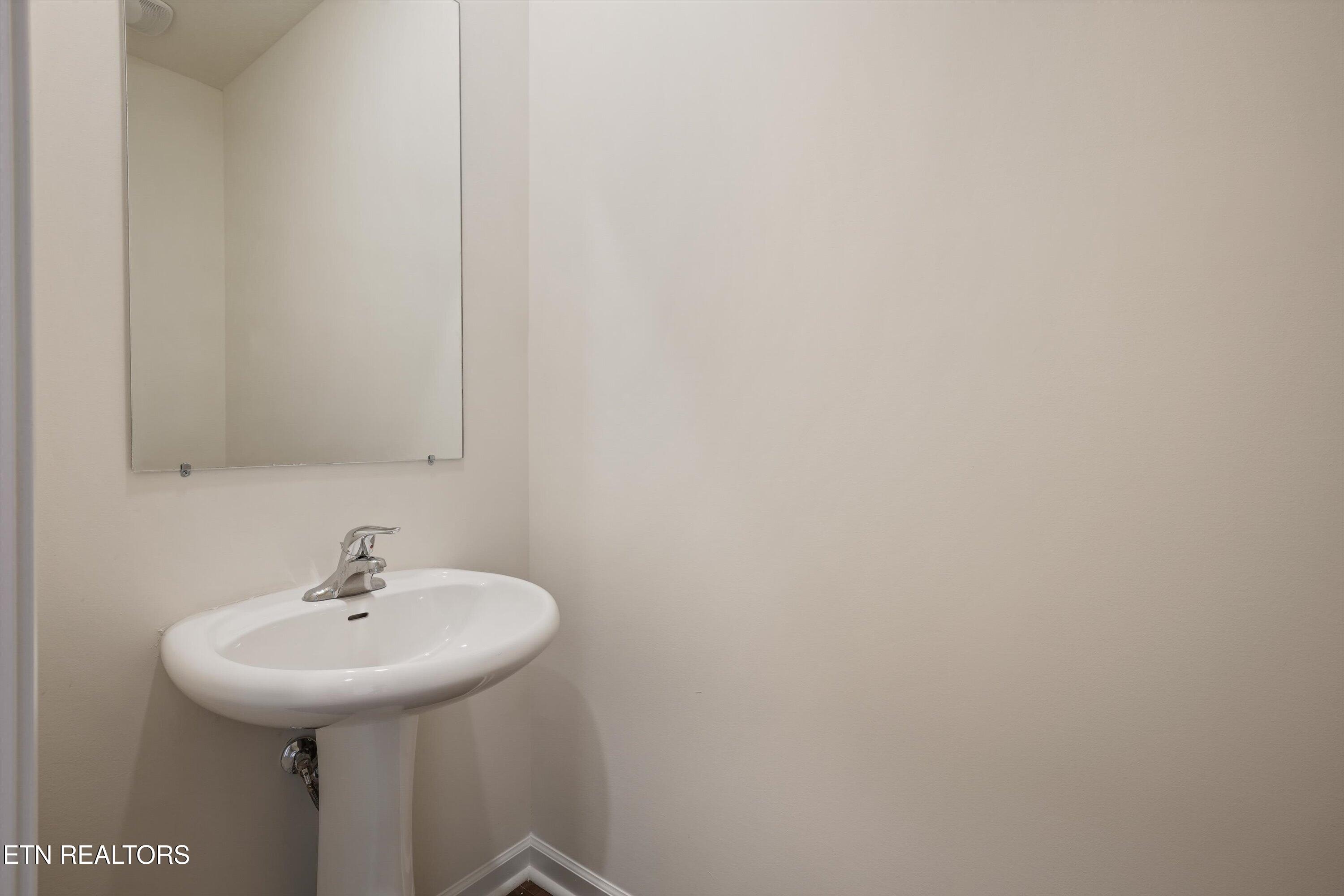 Bathroom pedestal sink with chrome faucet beneath a large frameless mirror.