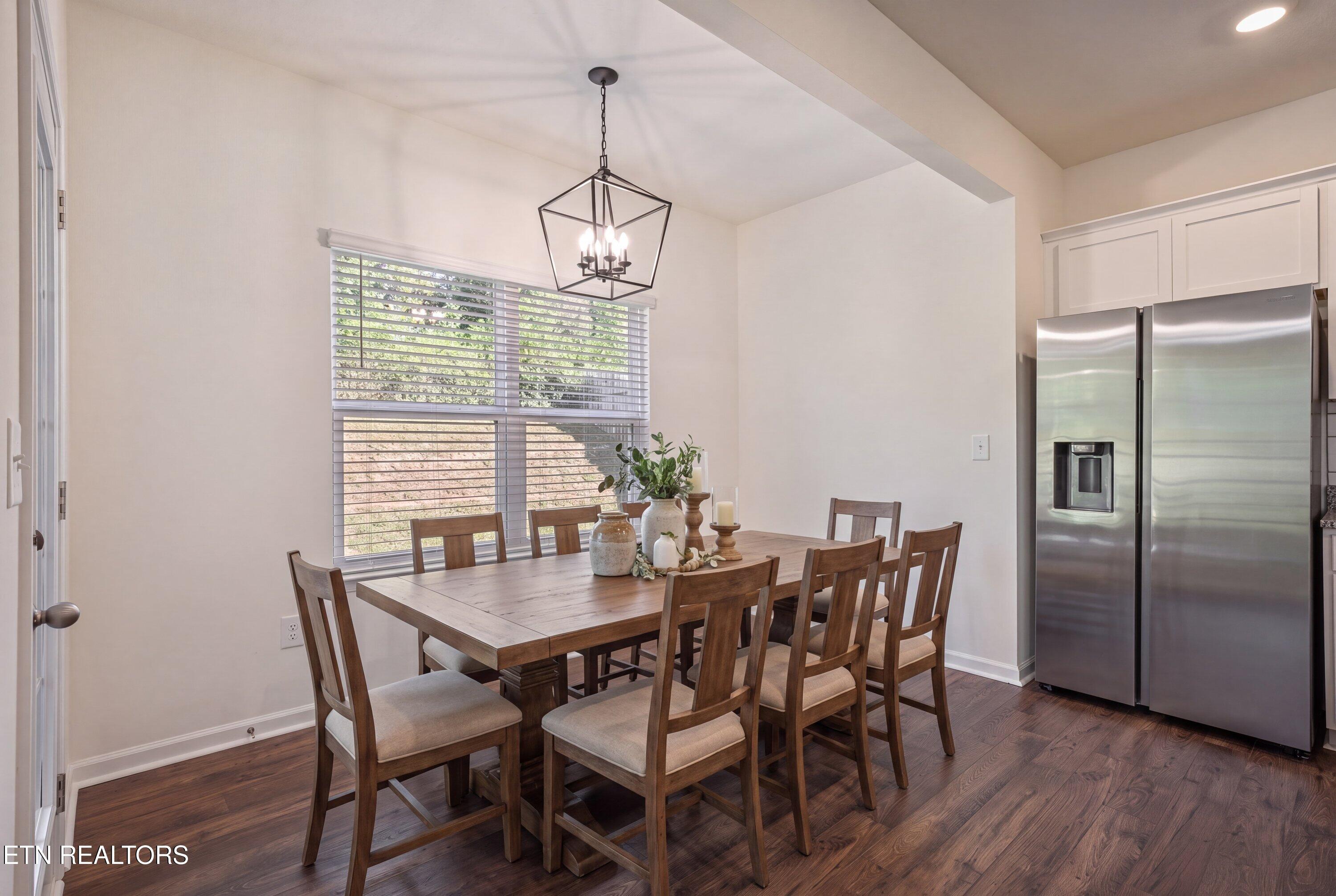 Dining area with a wooden table and chairs, geometric chandelier, wide window, and stainless steel refrigerator.