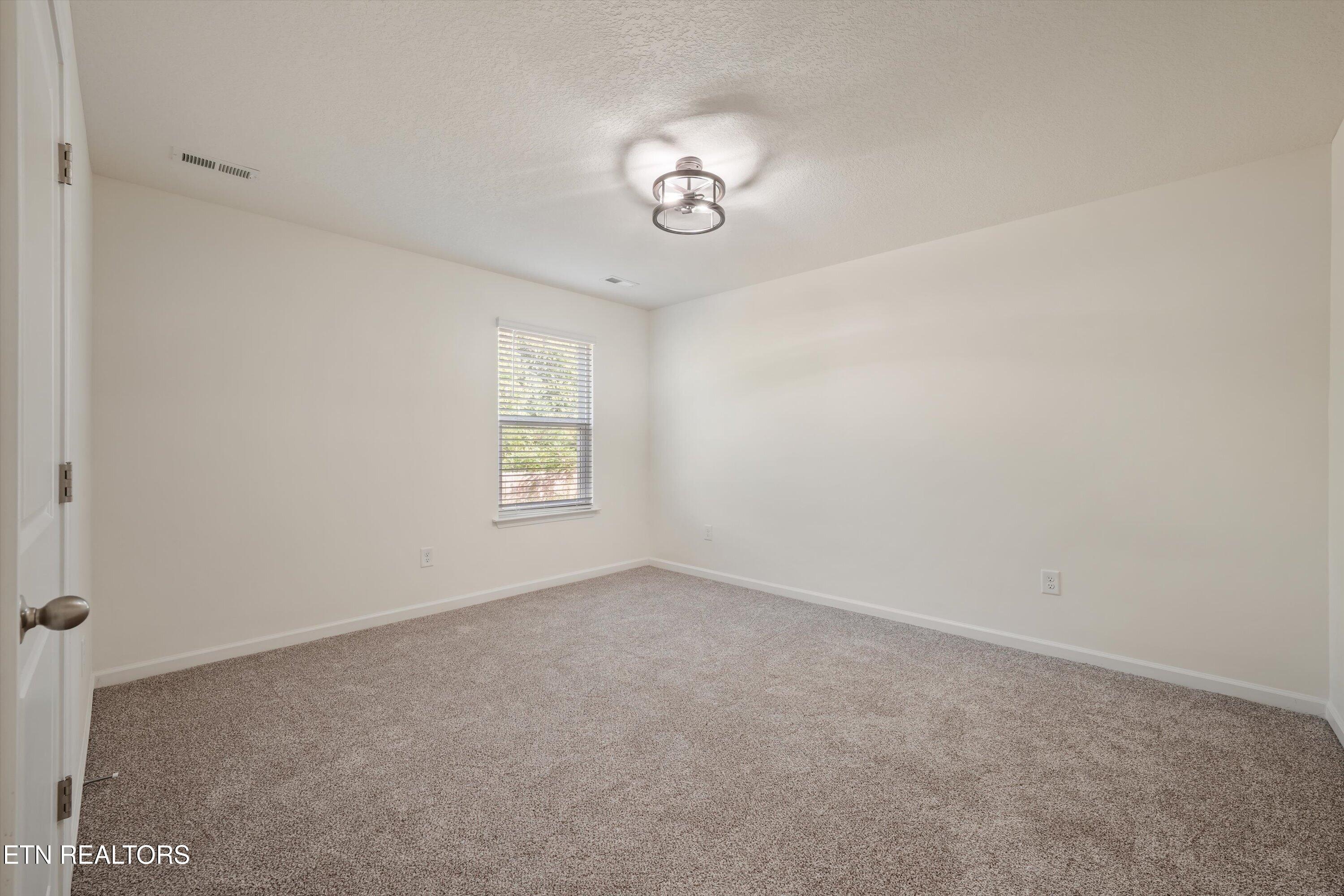 Empty bedroom with gray carpet, a window with blinds, and a modern ceiling light.