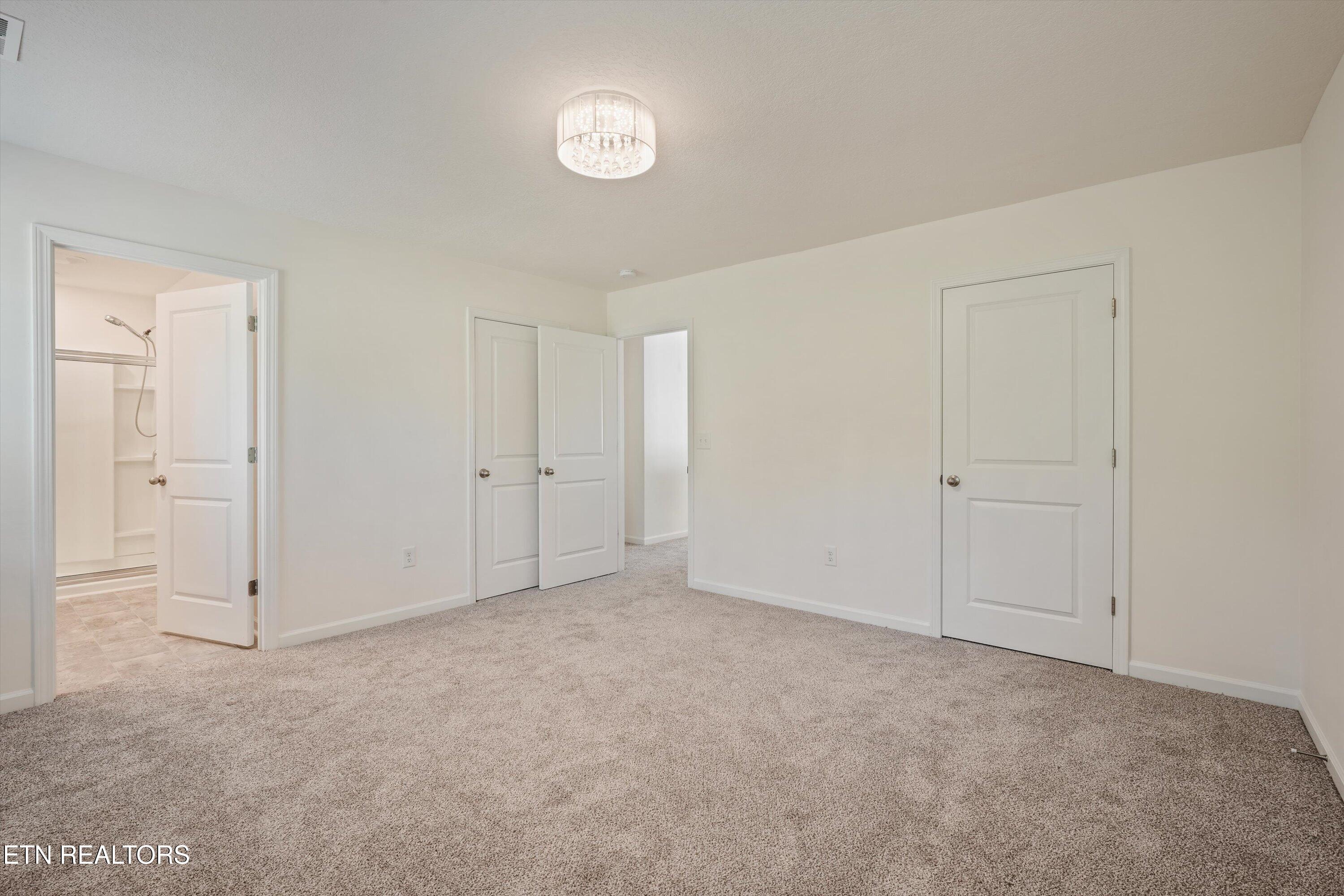 Empty carpeted bedroom with an open doorway to a bathroom and multiple white doors.