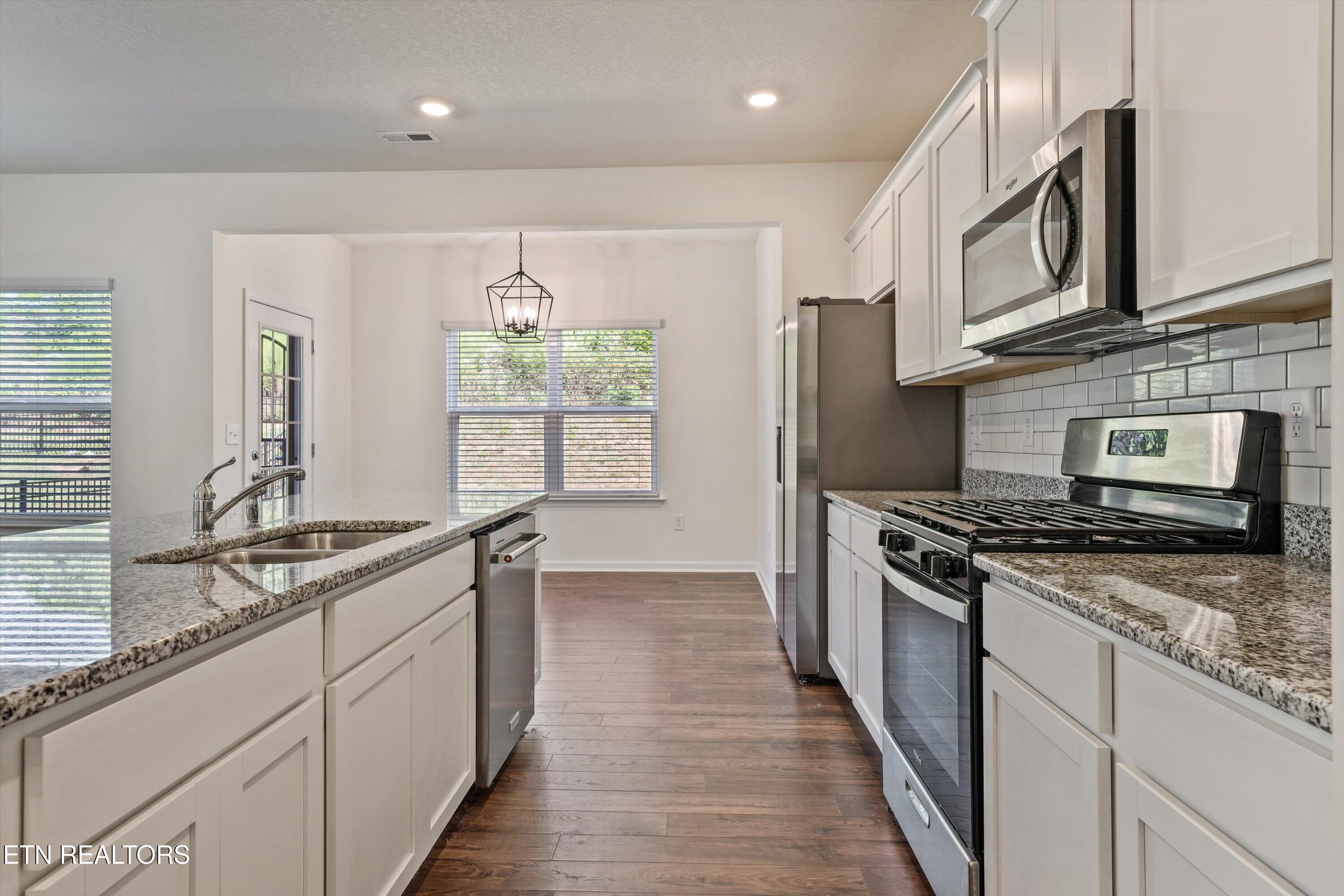 Kitchen with white cabinets, granite counters, a large sink island, and stainless steel appliances.