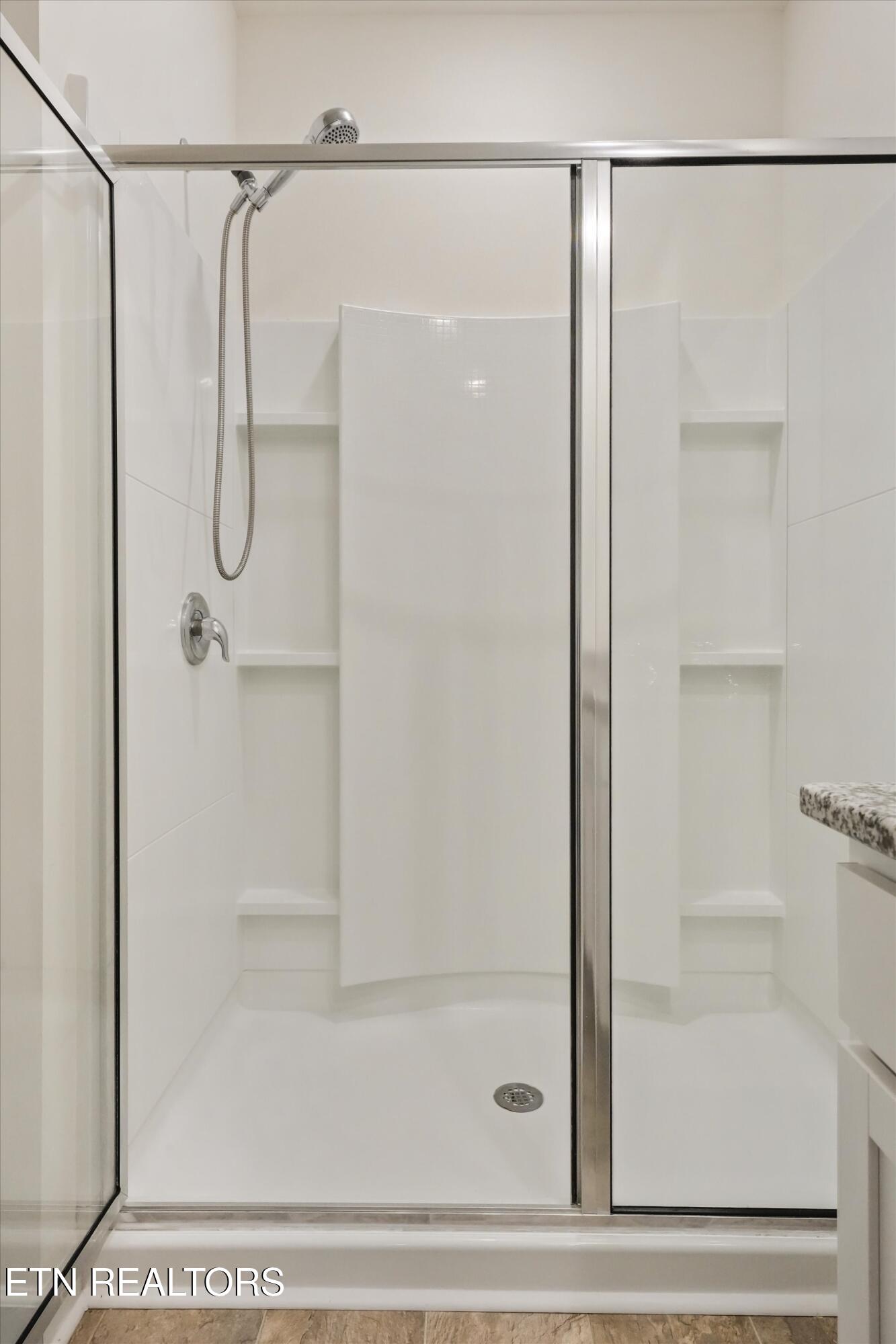 Walk-in shower with sliding glass doors, built-in shelves, and a handheld showerhead.