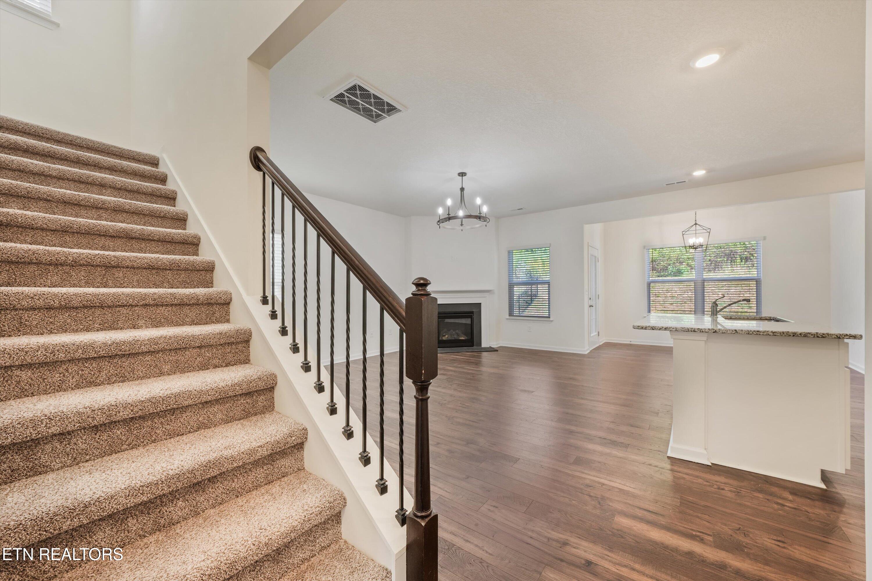 Open-plan interior with carpeted stairs, dark railing, fireplace, and kitchen island.