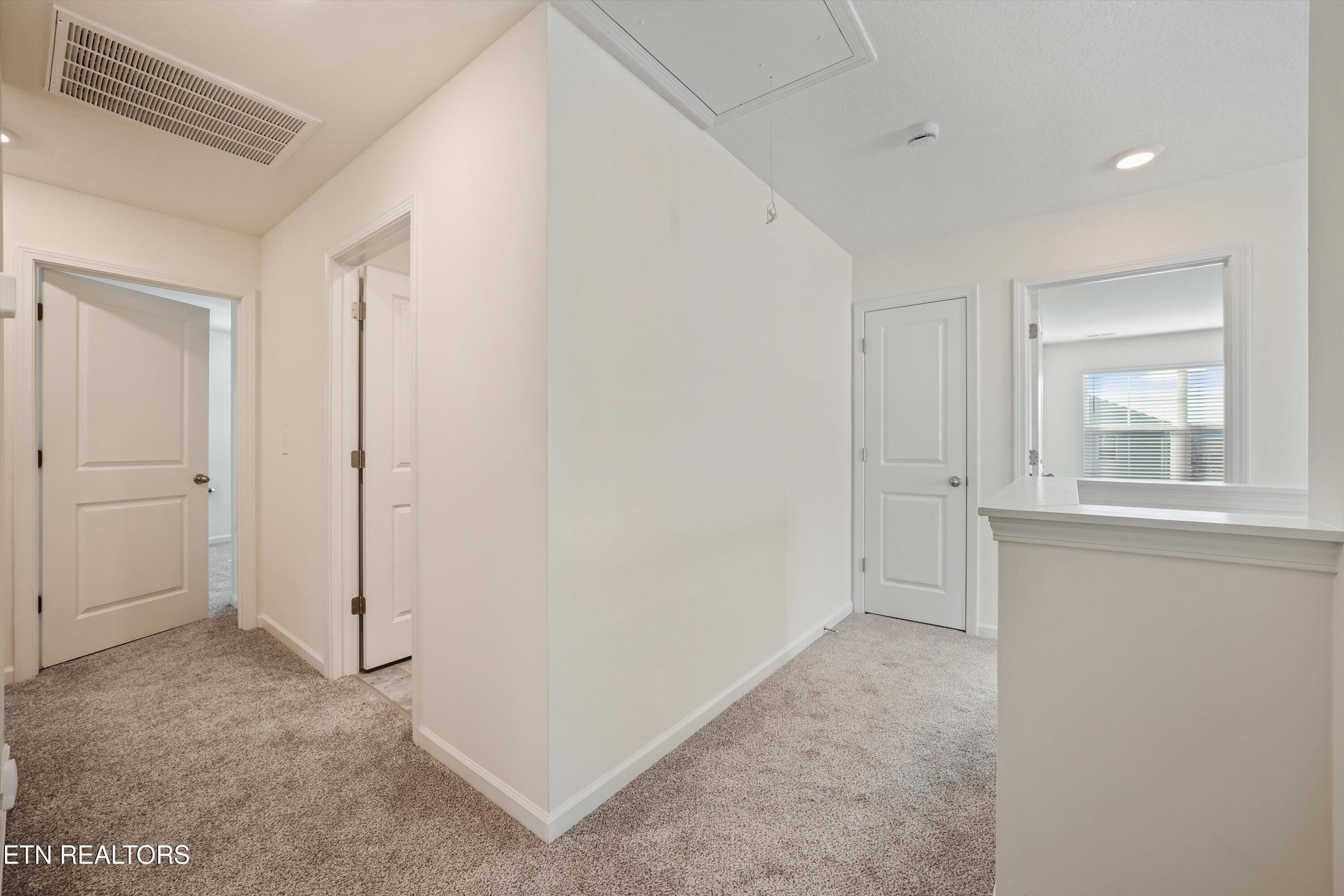 Carpeted hallway with white paneled doors and a half-wall overlooking a counter.