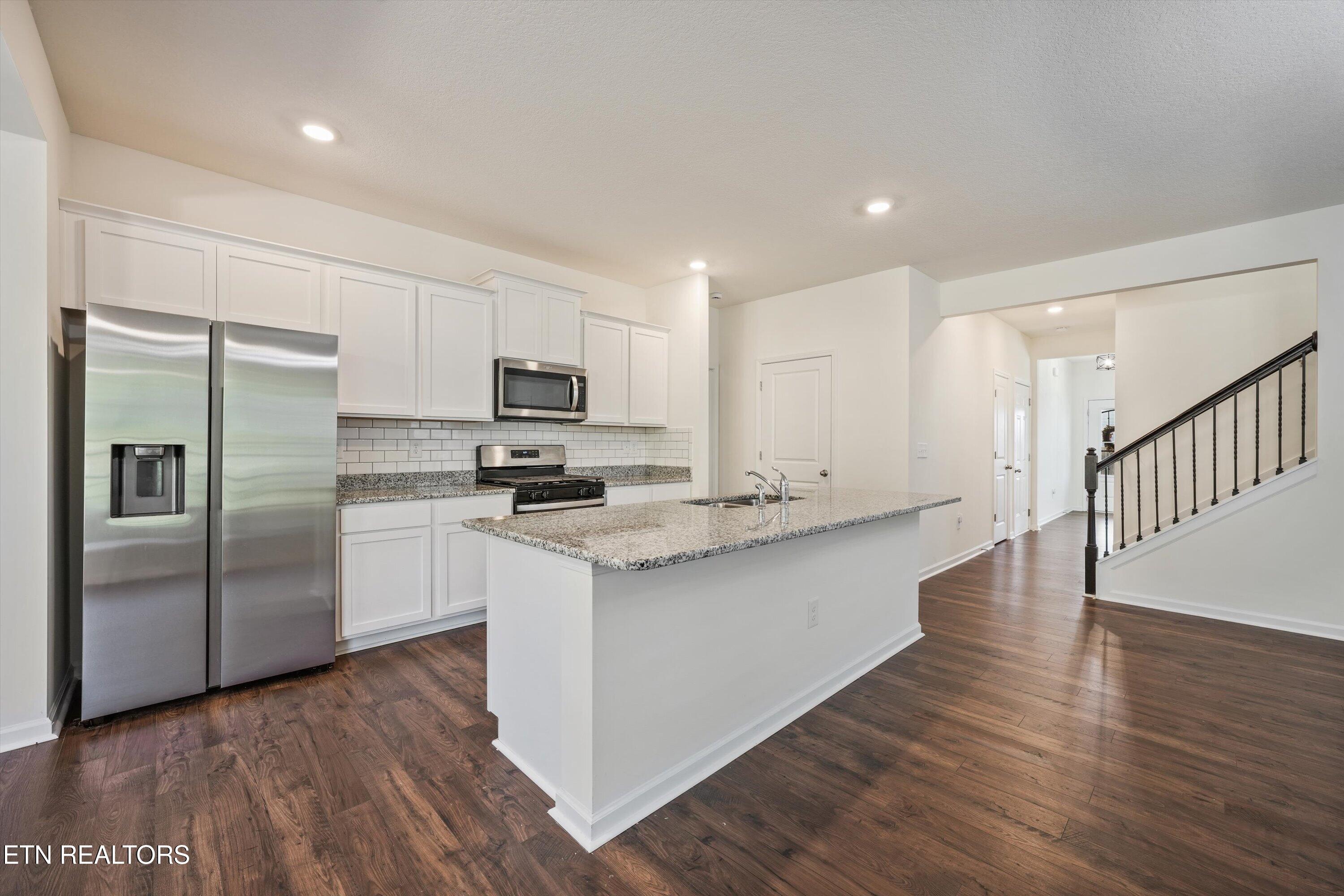 Unfurnished kitchen with white cabinets, stainless steel appliances, granite island, and dark wood floors.