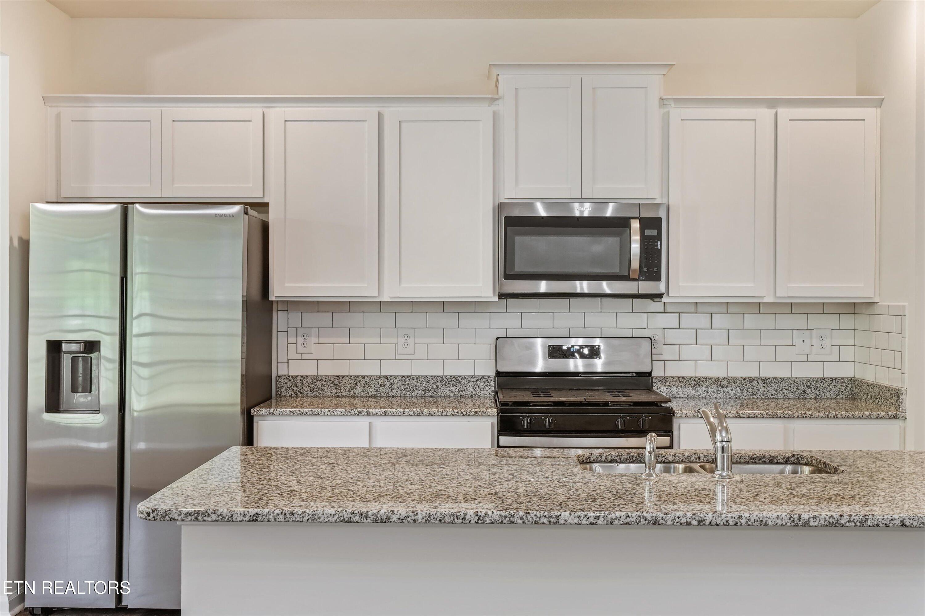 Kitchen with white cabinets, stainless steel appliances, granite counters, and a large island sink.