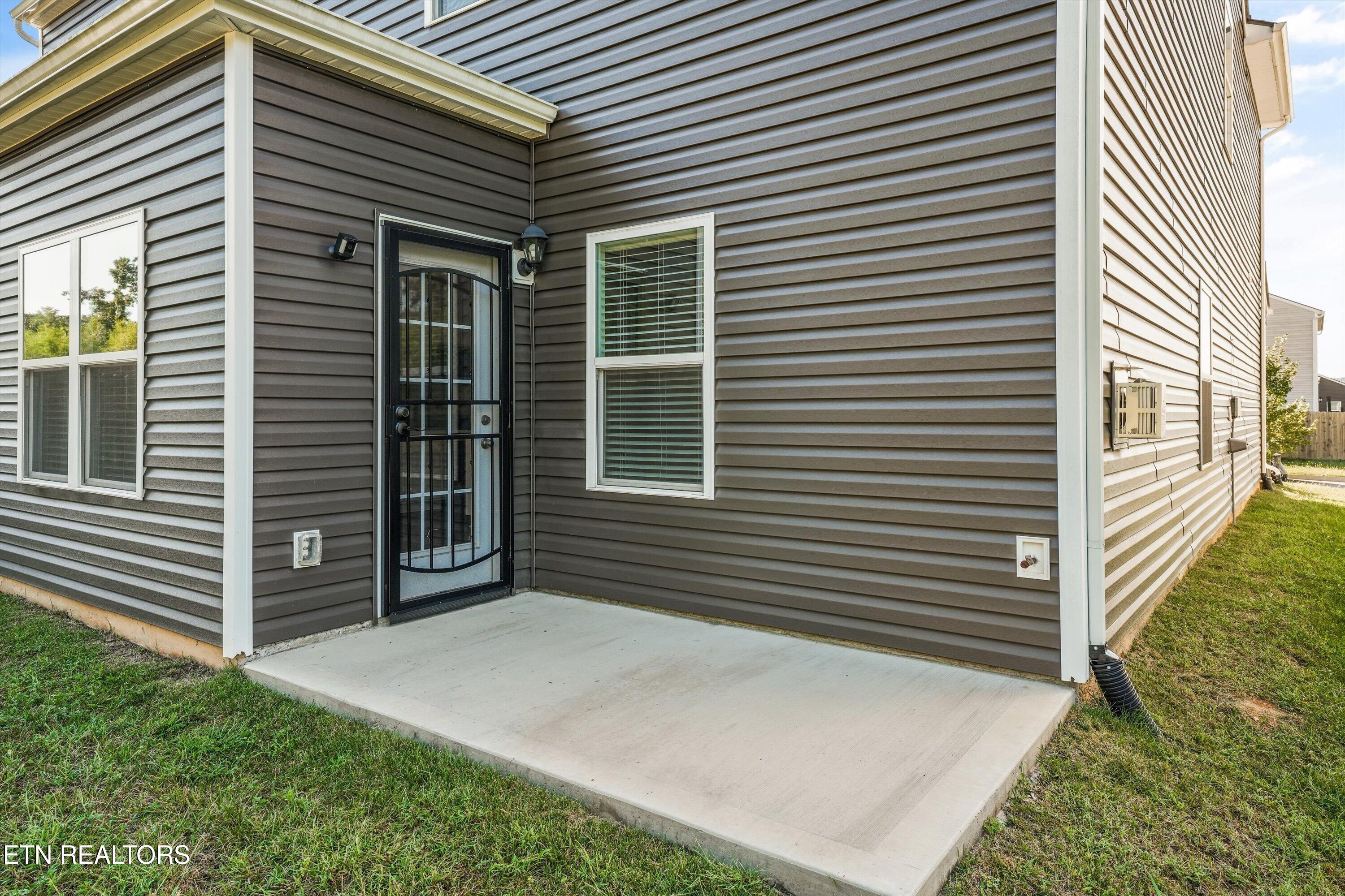 Gray-sided home with a black security door opening onto a concrete patio.