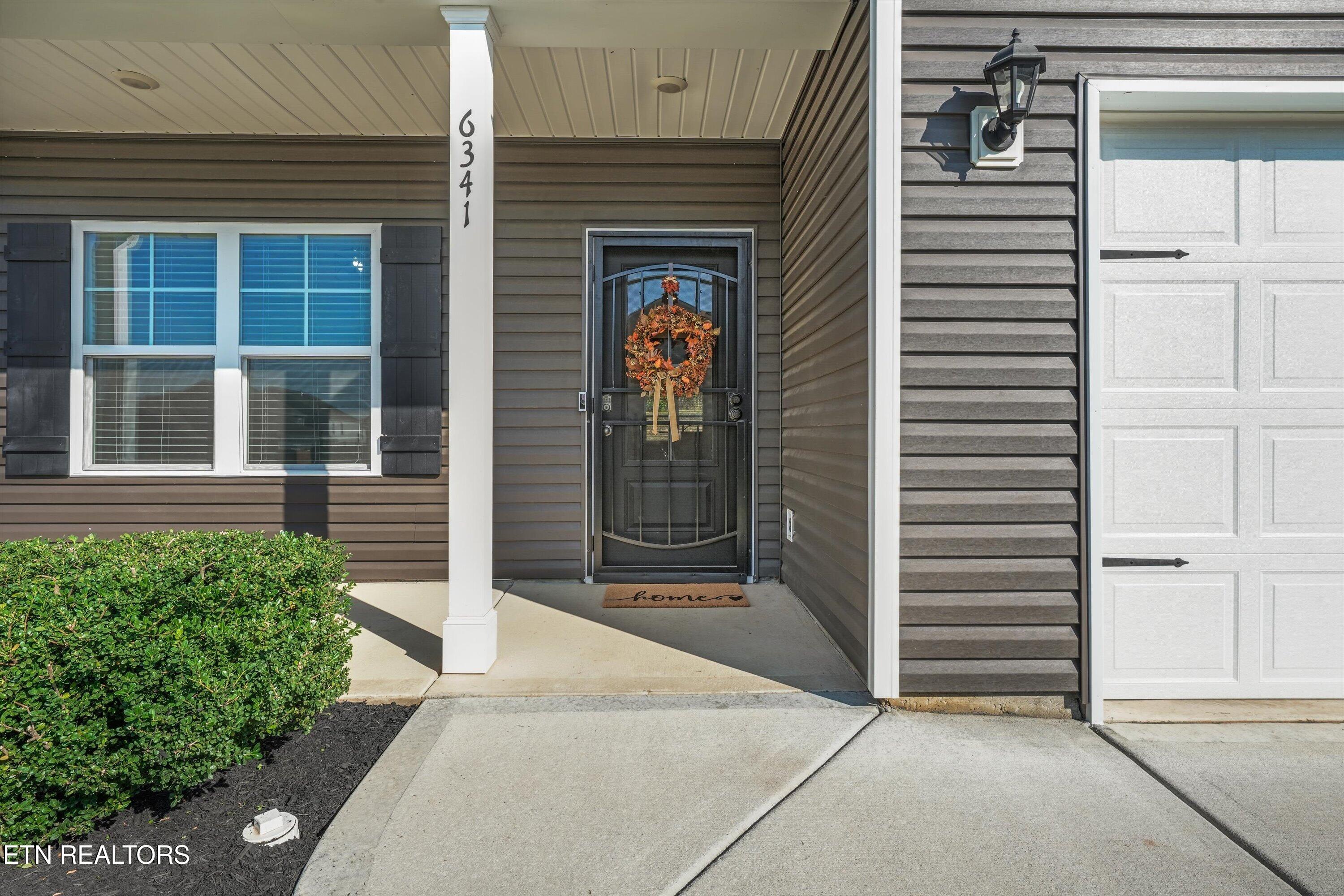 Home entrance with an autumn wreath on the dark front door, covered porch, and attached garage.