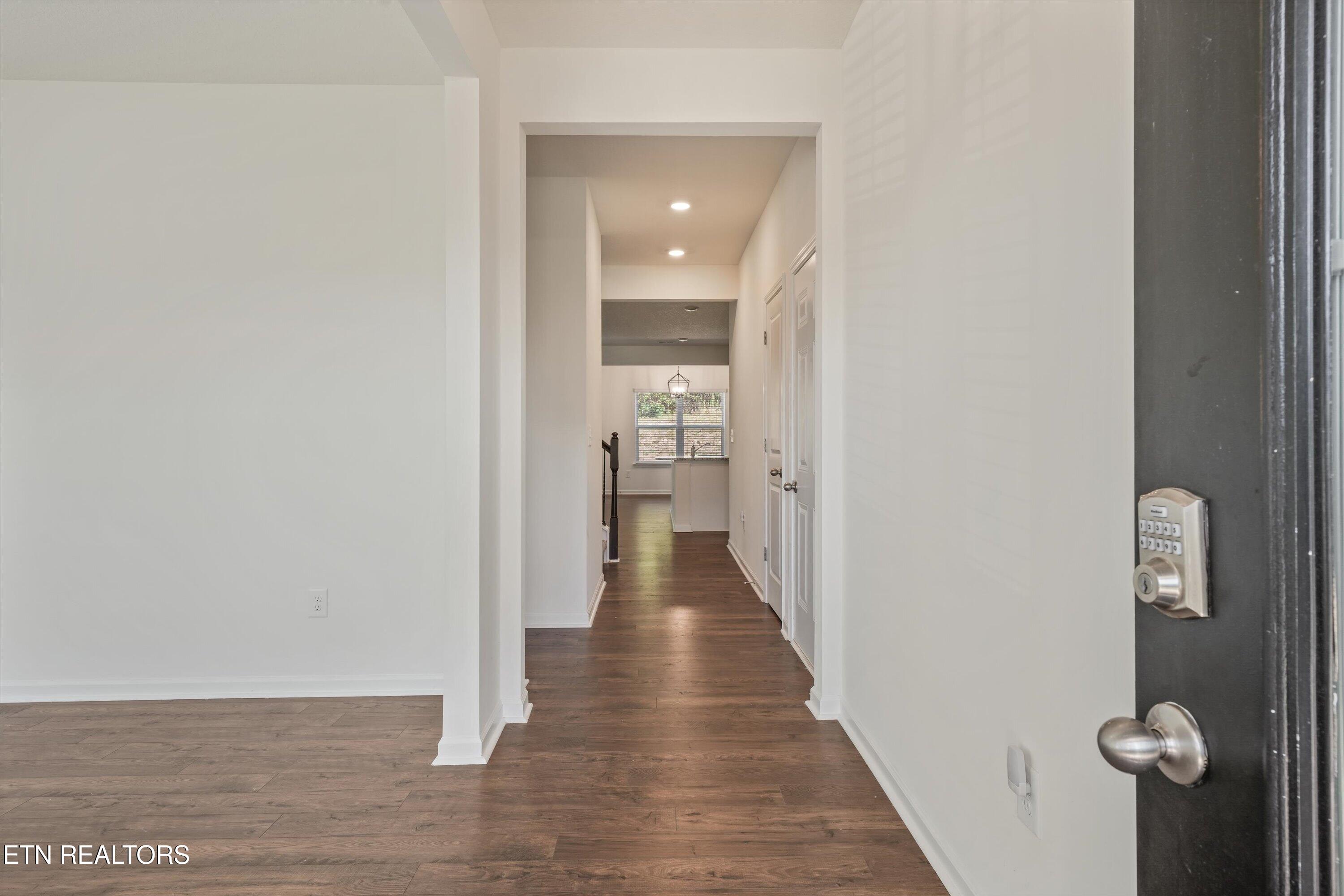 Open front door looking down a bright hallway with dark wood floors and a window at the far end.